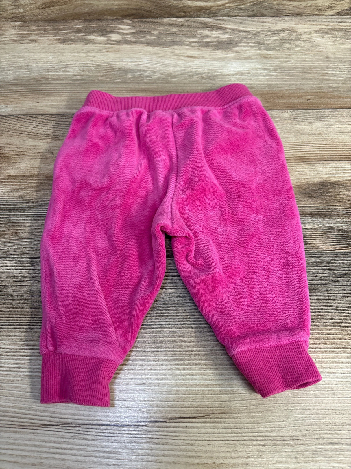 Pink velour baby pants with ribbed cuffs on wood background