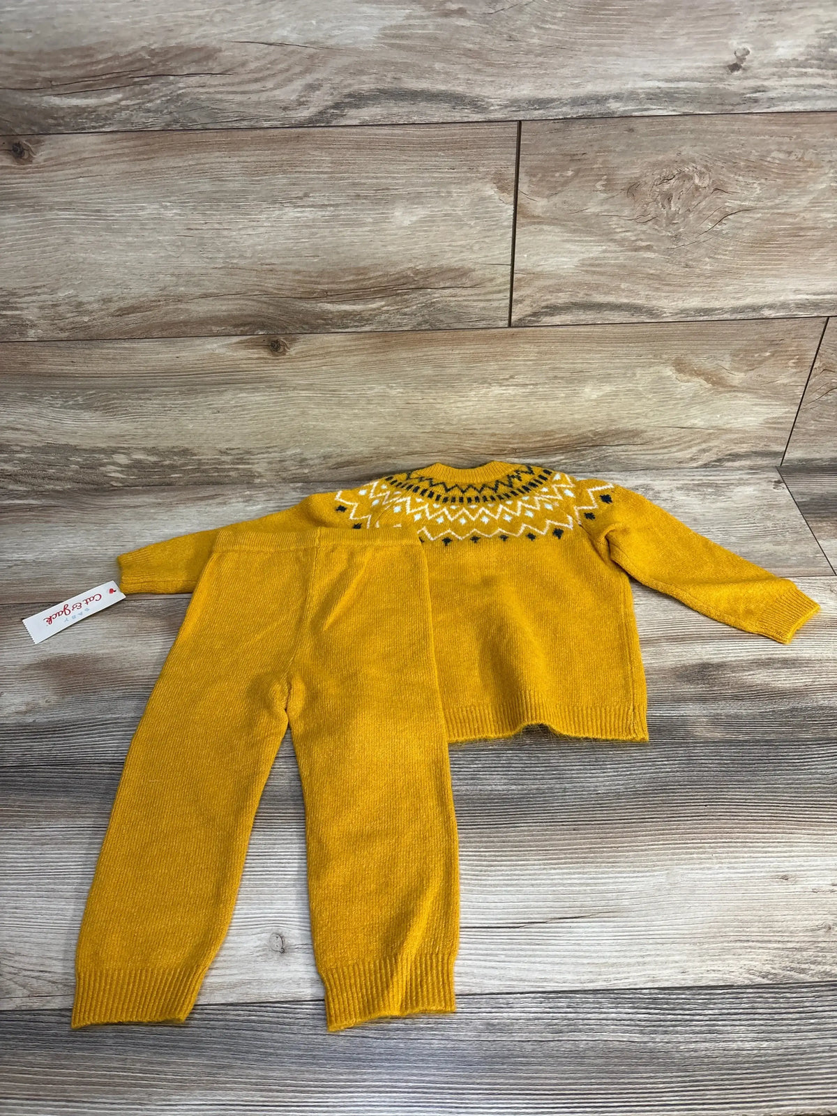 Yellow knit baby sweater and pants set with patterned neckline on wood background