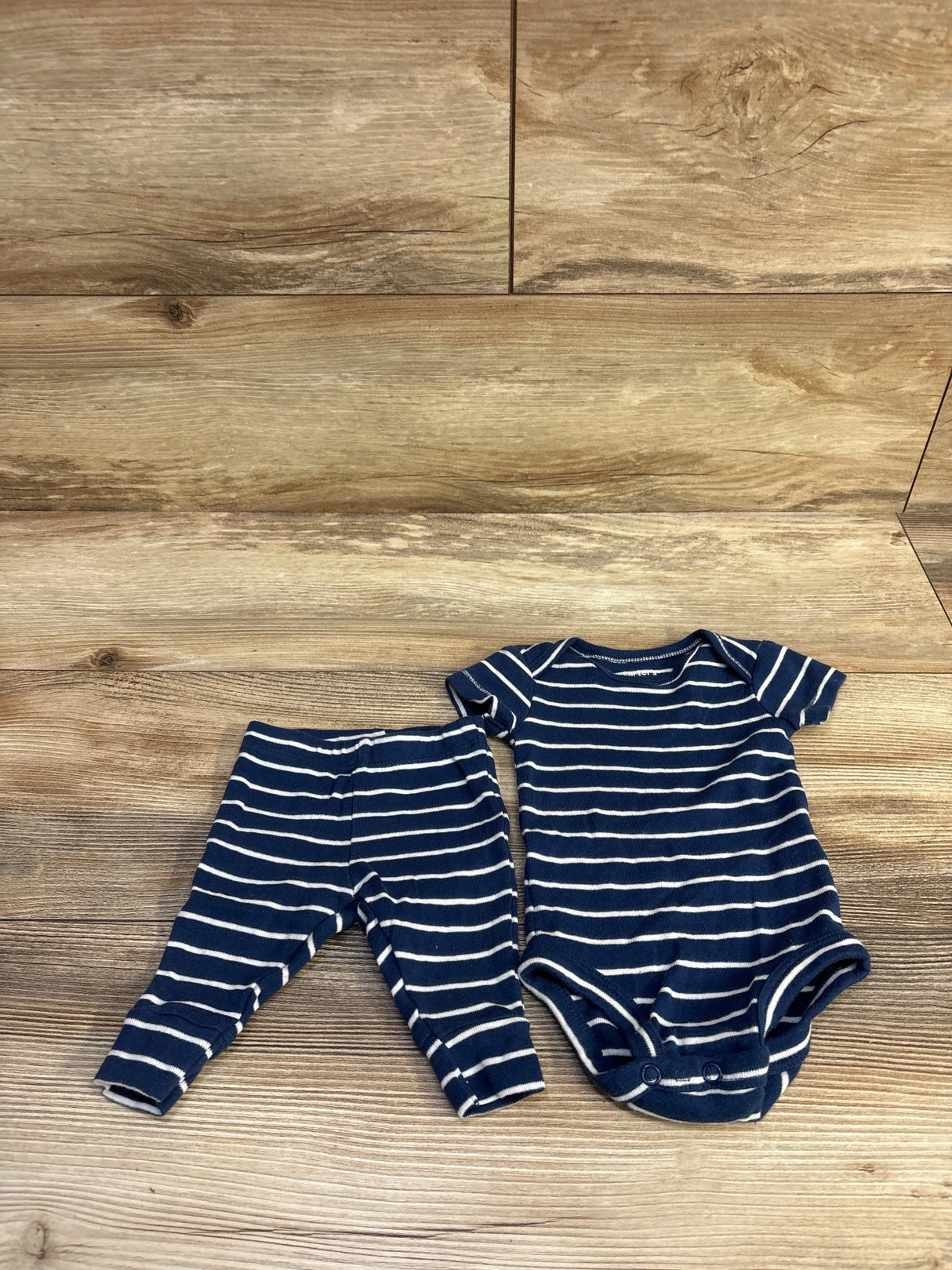 Flat lay of Carter’s newborn navy-and-white striped bodysuit with snaps and matching pants on wood background