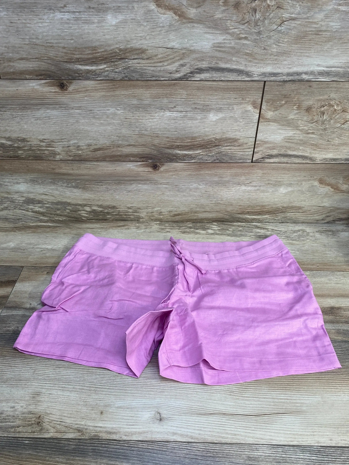 Front view of pink maternity linen-cotton shorts showing elastic drawstring waistband, flat on wood background