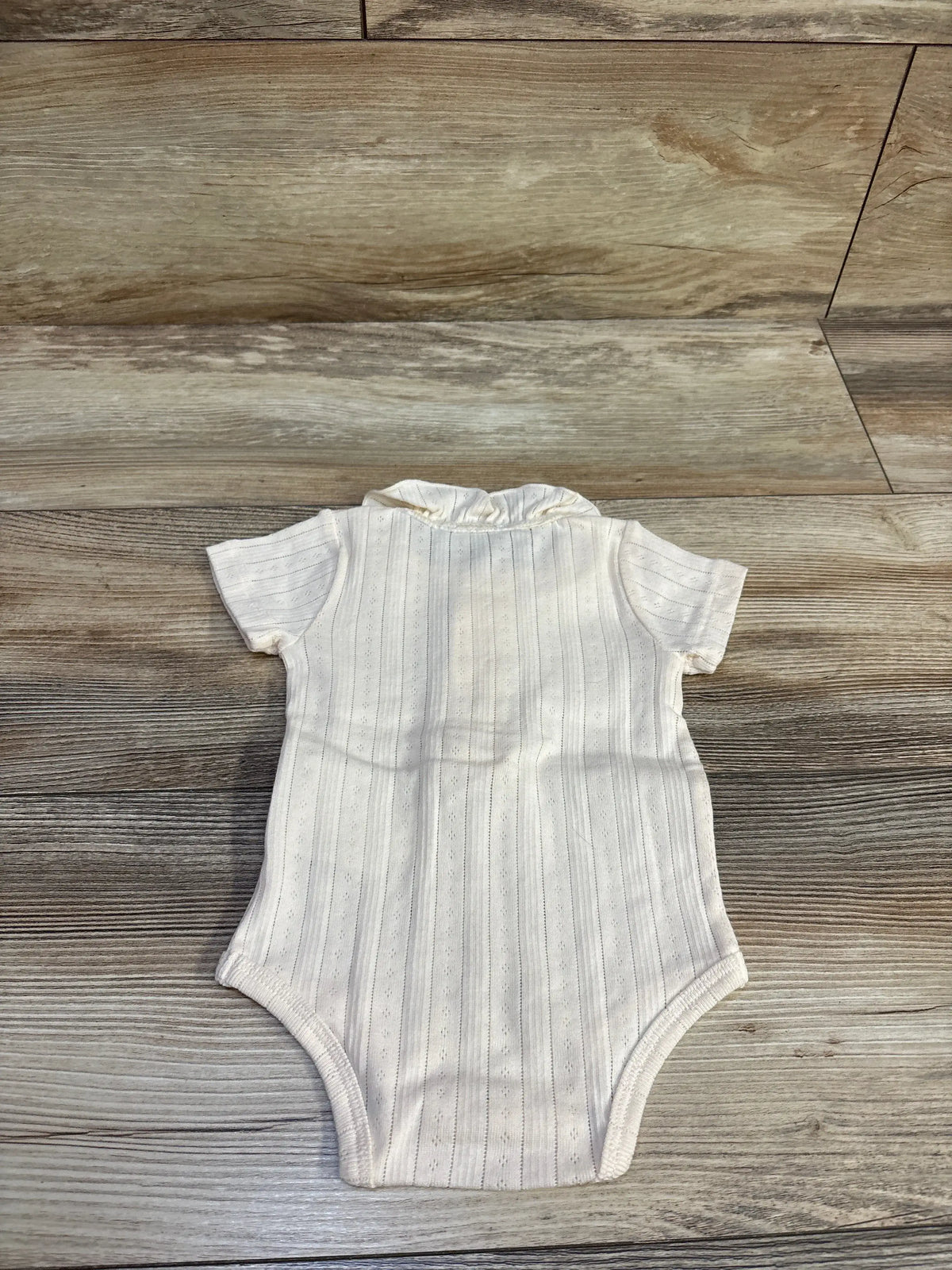 Flat-lay back view of Bout’Chou ivory pointelle knit bodysuit with ruffled collar and vertical eyelet stripes on light wood
