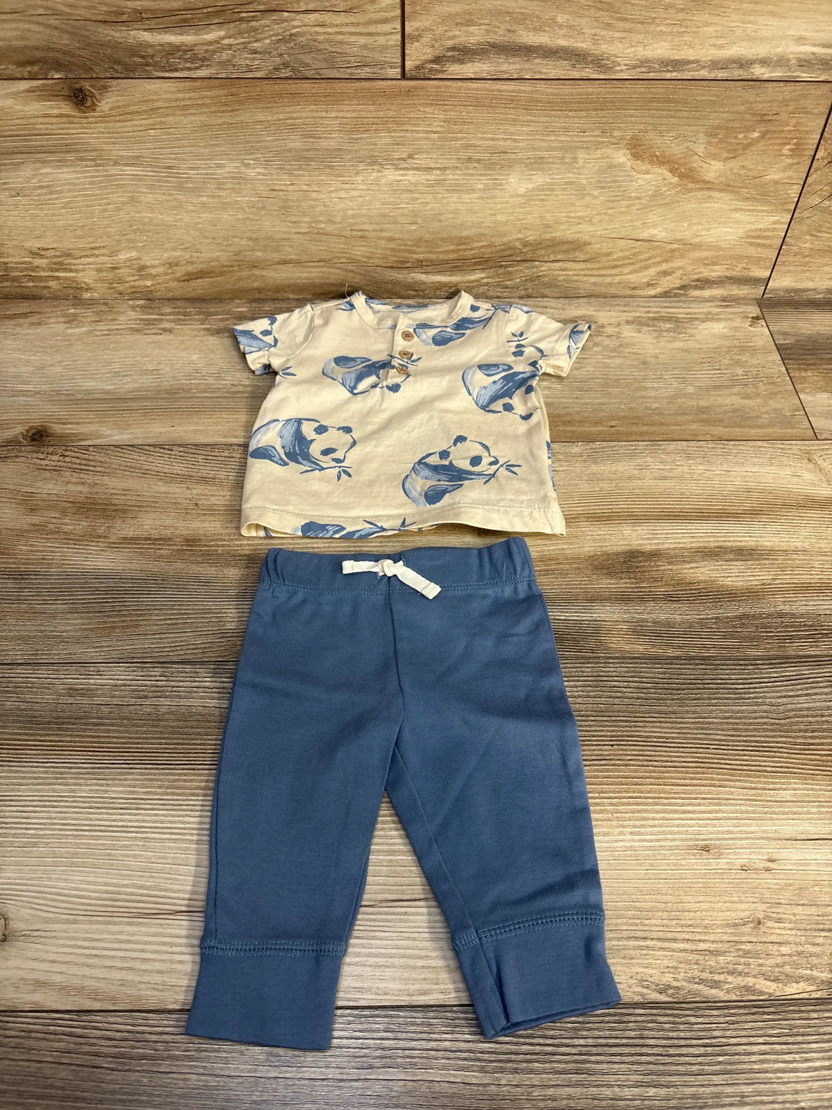 Top view of Carter’s two-piece baby clothing set showcasing panda-print beige henley shirt and blue pants on wood flooring