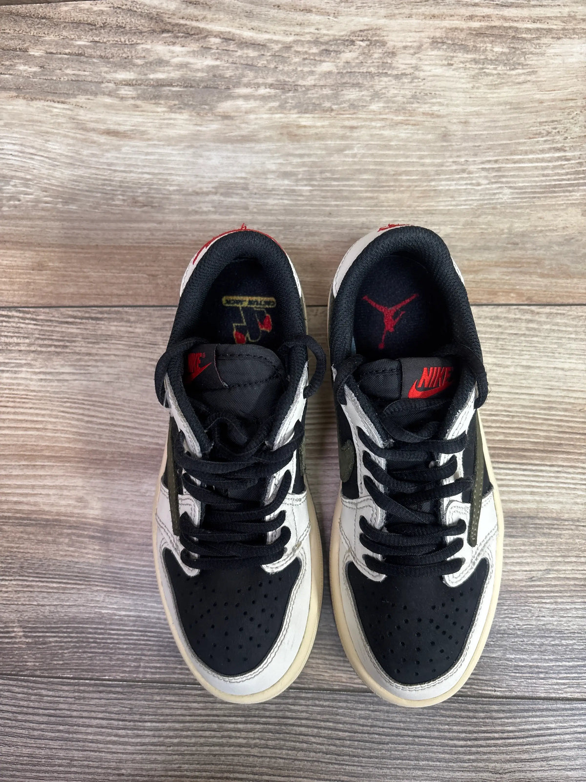 Top view of Travis Scott x Air Jordan 1 Retro Low OG SP PS Olive sneakers showcasing black, olive, and white panels on wood-grain flooring