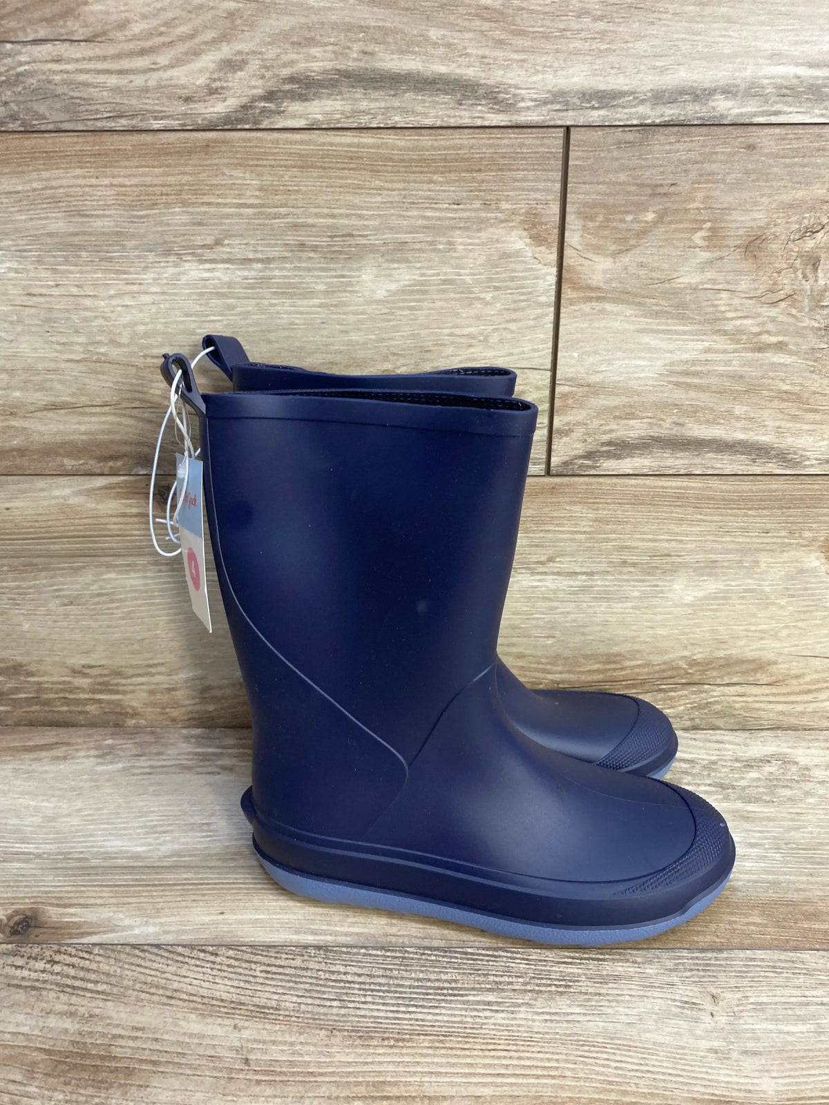 Side view of Cat & Jack navy slip-on children’s rain boots showcasing pull tabs and textured toe with wood plank background
