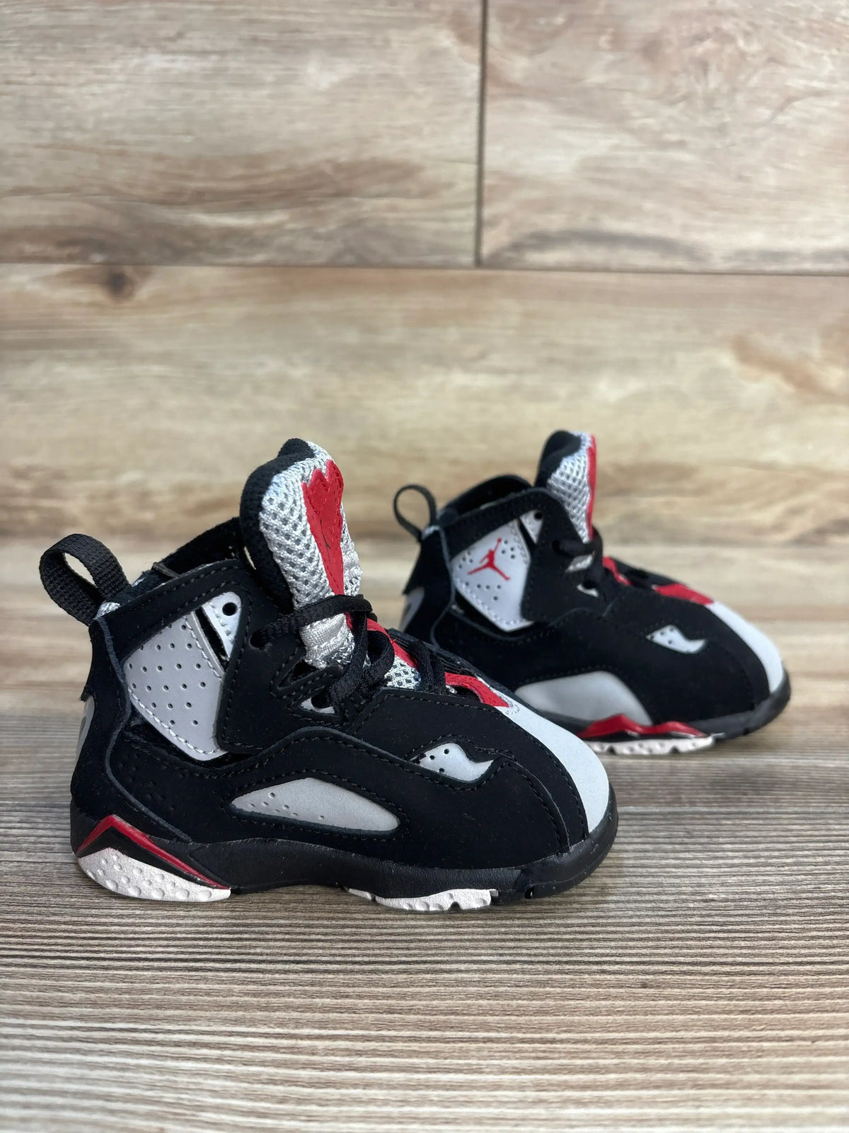Black, white, and red toddler athletic shoes on wooden floor, gently used condition