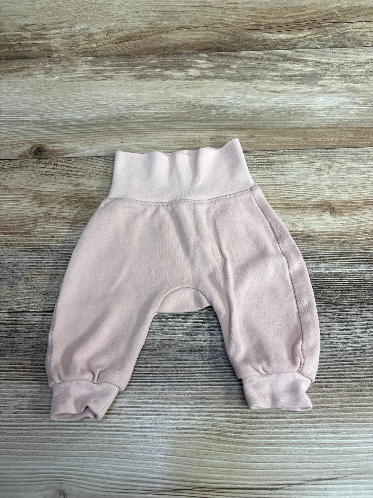Soft pink baby pants with cuffed ankles and elastic waistband on wooden floor