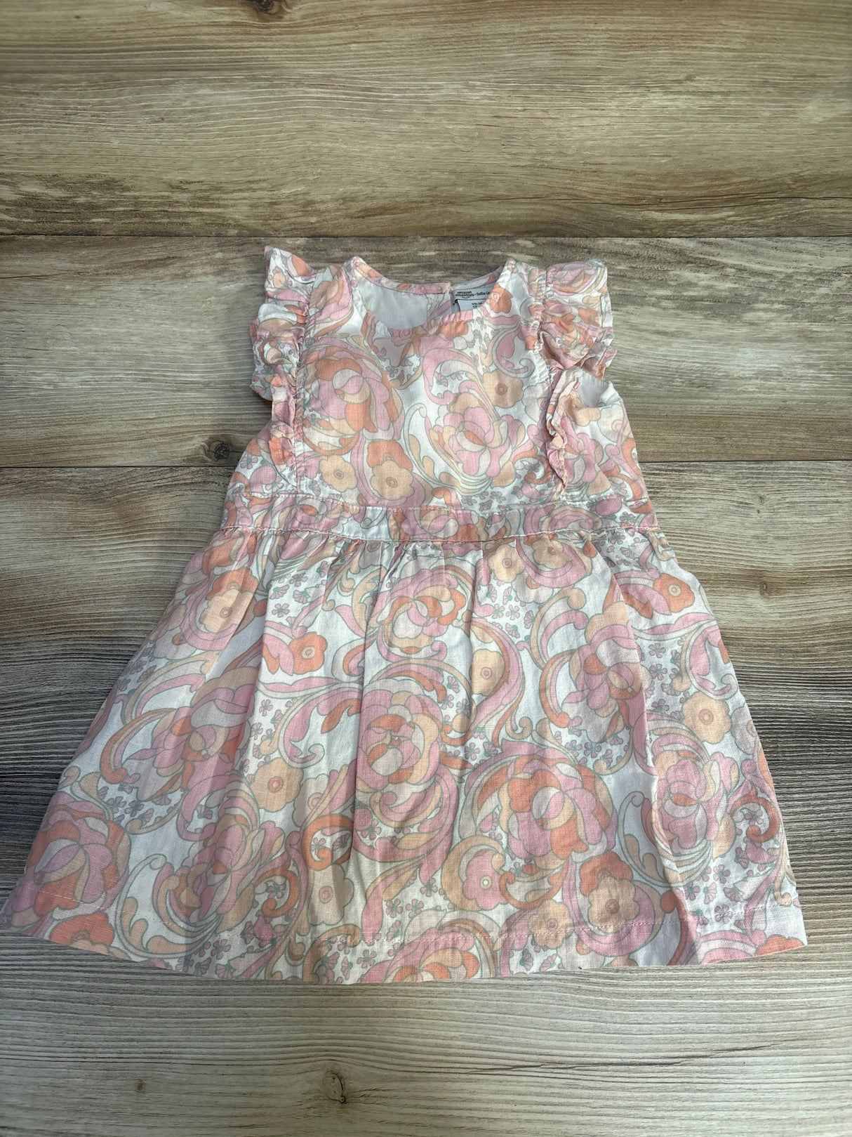 Floral print baby dress with ruffled sleeves in peach and pink on wood background