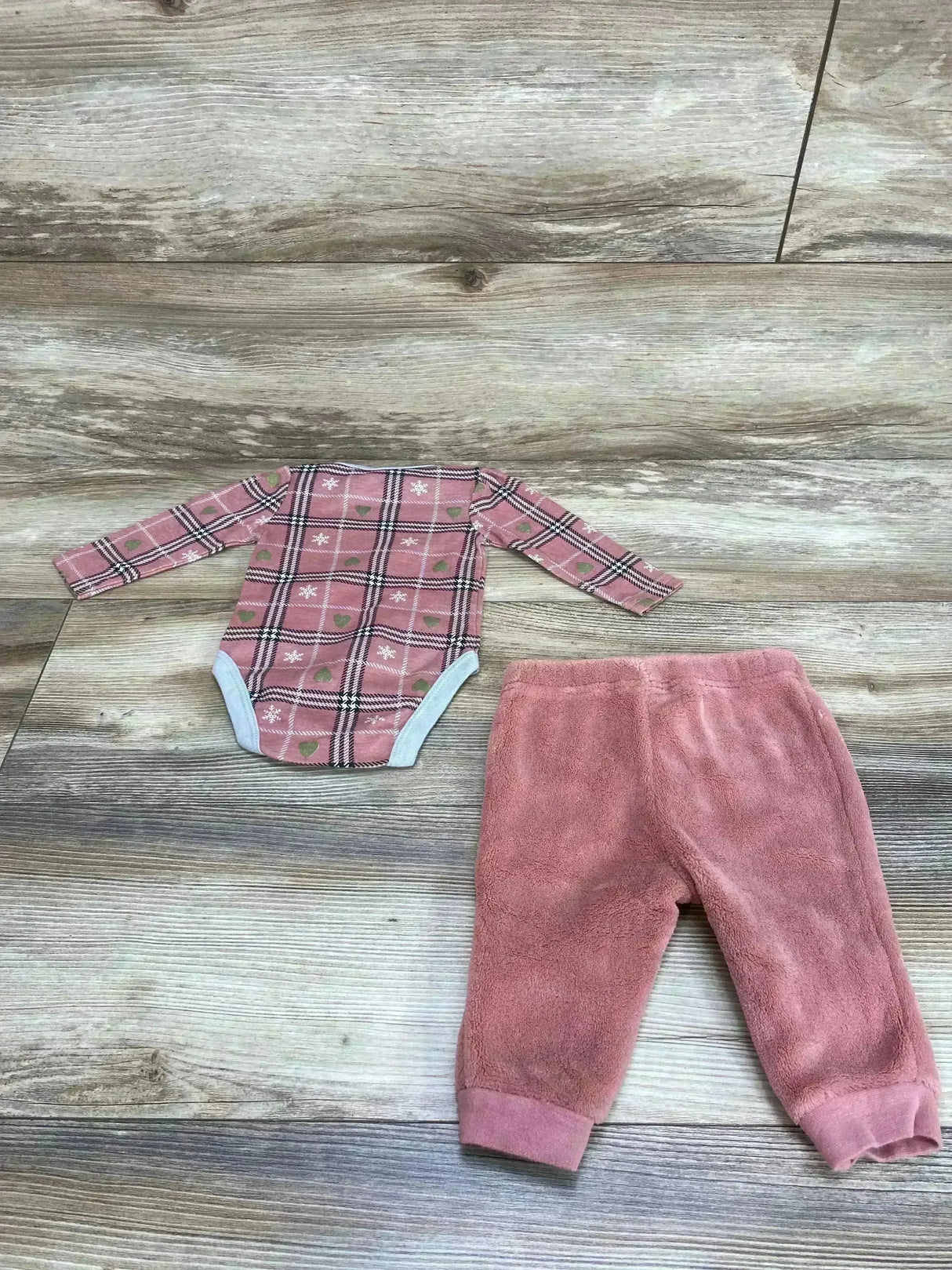 Flat-lay of Rudolph Red-Nosed Reindeer bodysuit and pink plush pants showing plaid print and cuffed ankles on wood