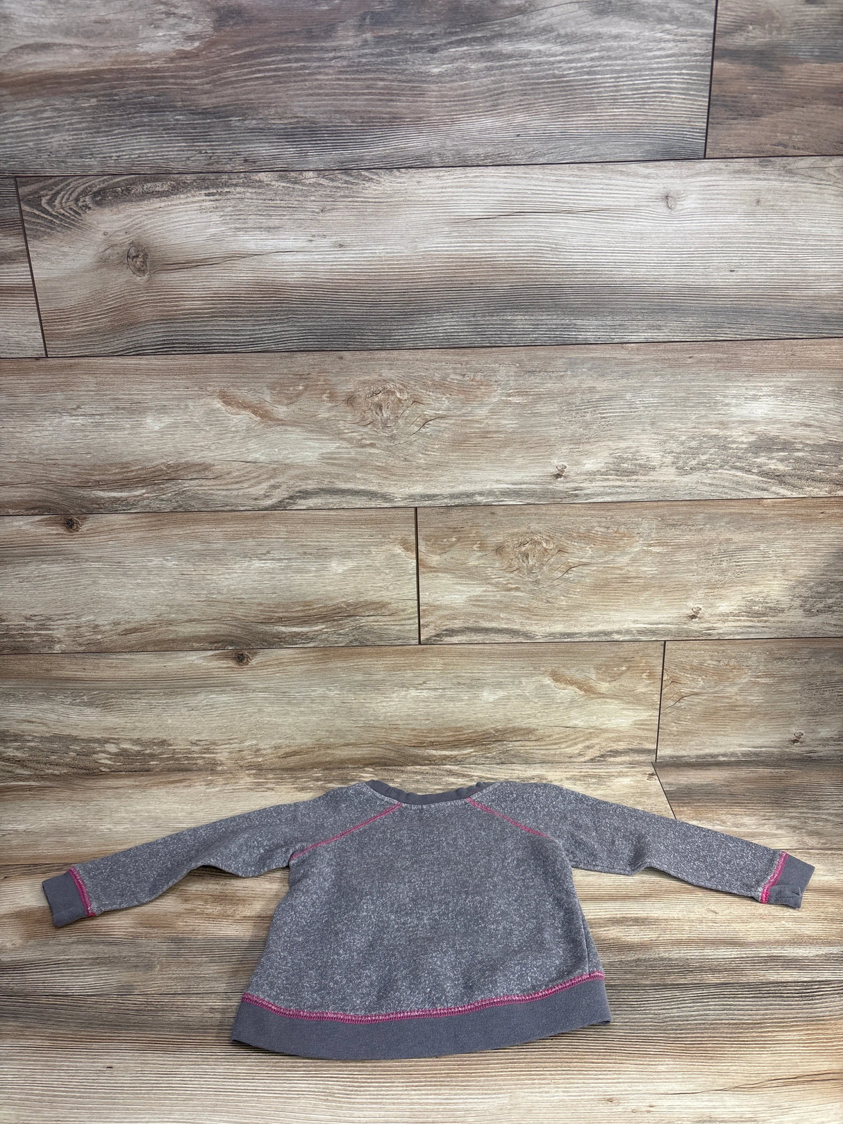 Kids long sleeve gray sweatshirt with pink stitching on wood floor background
