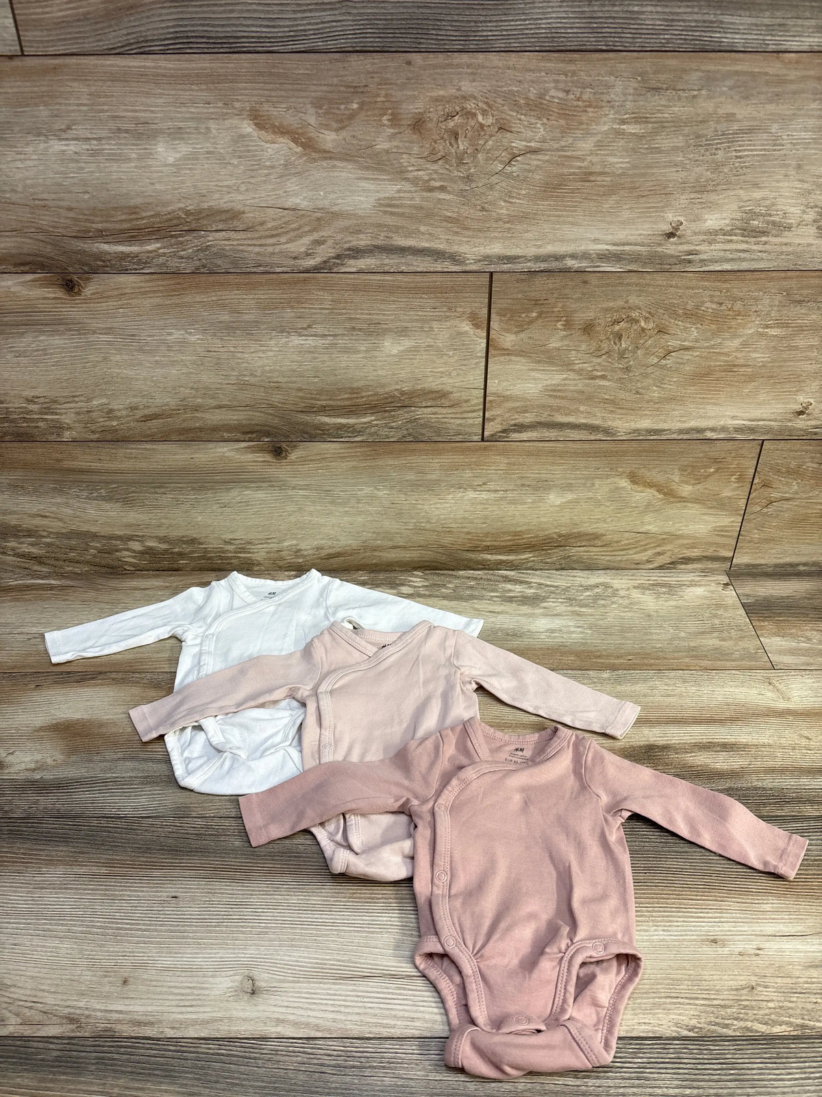 H&M Organic 3-pack wrapover bodysuits in white and pink shades on a wood background.