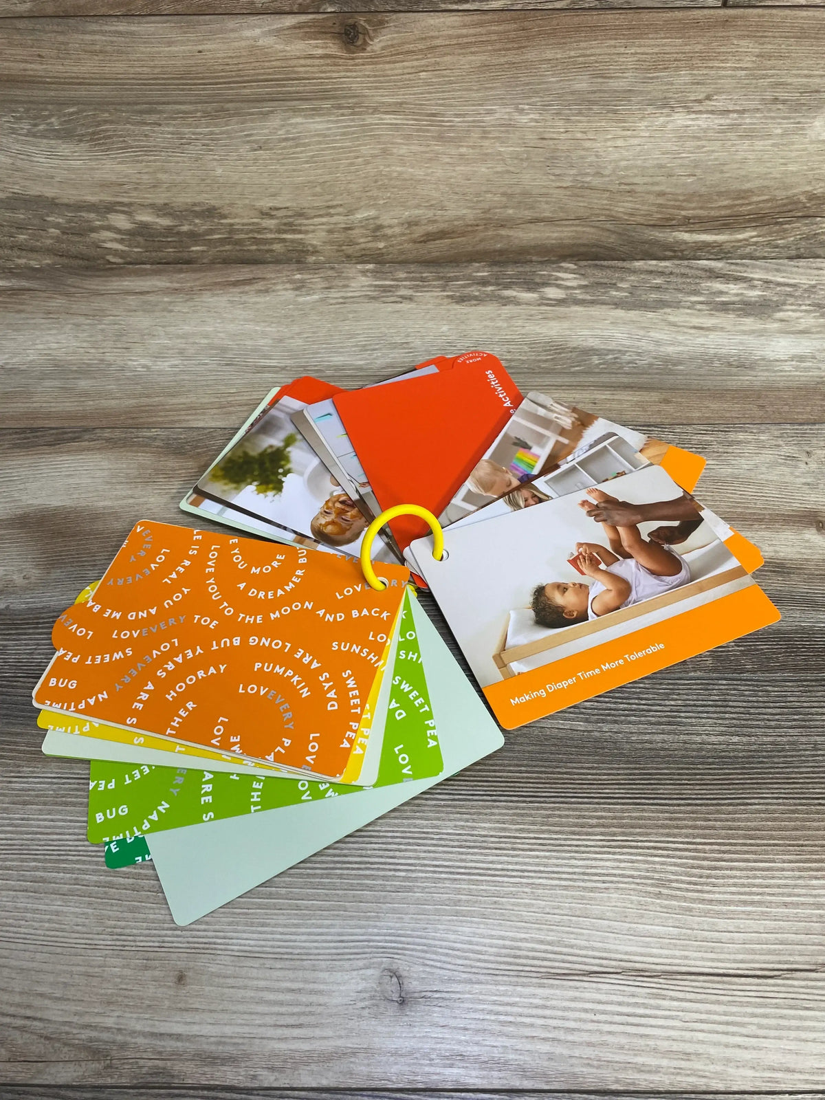 Fanned view of Lovevery The Thinker play guide cards on a yellow ring, showing colorful activity and diaper time tip cards on a wood surface