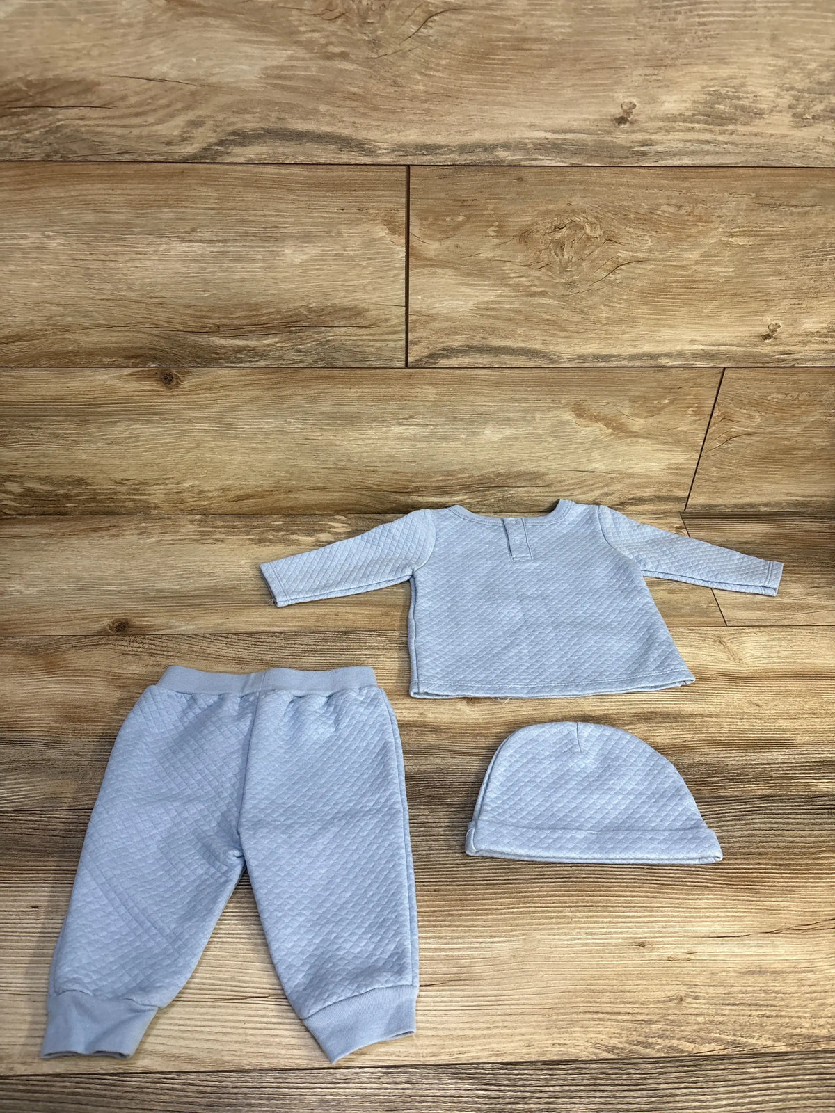 Top view of Sterling Baby 3pc Lil’ Cowboy Set in blue showcasing quilted shirt, pants, and hat on a wood floor