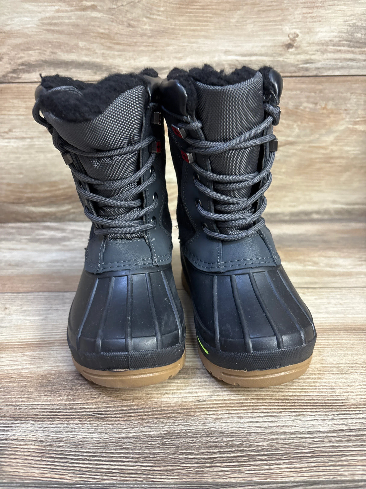 Front view of child black Swiss Tech winter boots showing faux fur lining laced shaft rubber toe and brown sole on wood floor