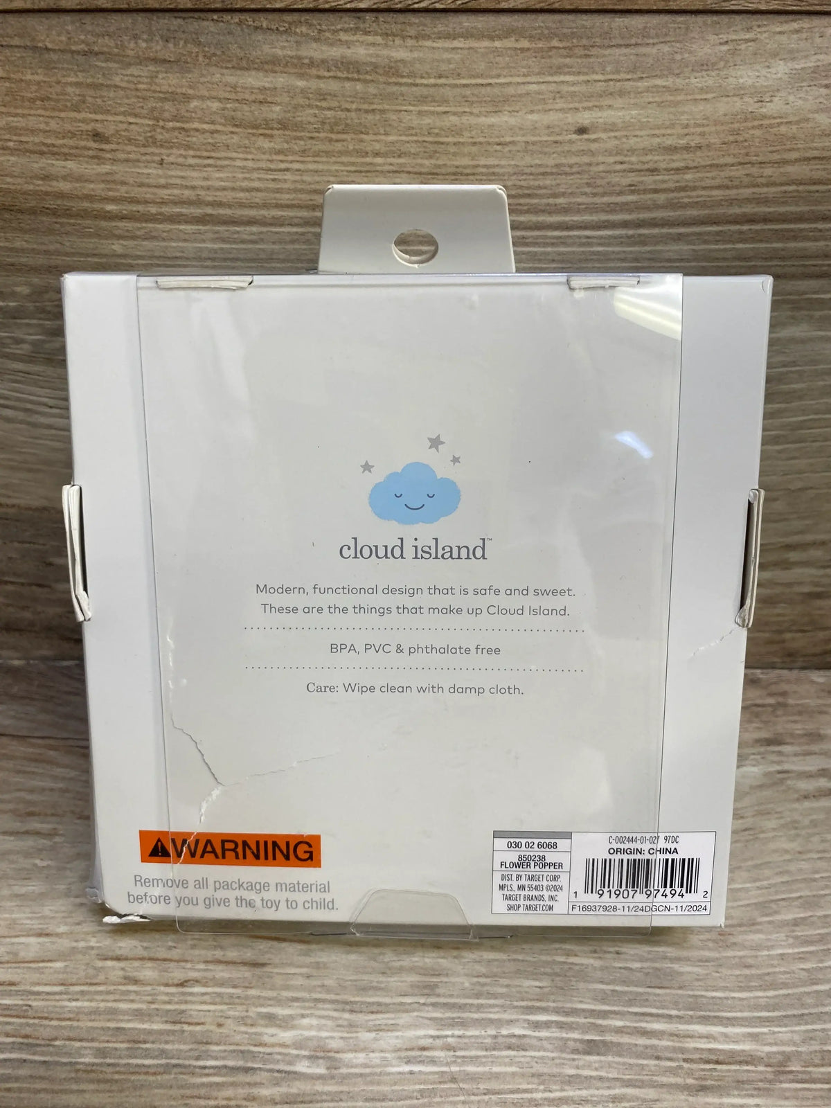 Rear view of Cloud Island silicone popper toy box showing logo, safety text, orange WARNING label and barcode on wood background