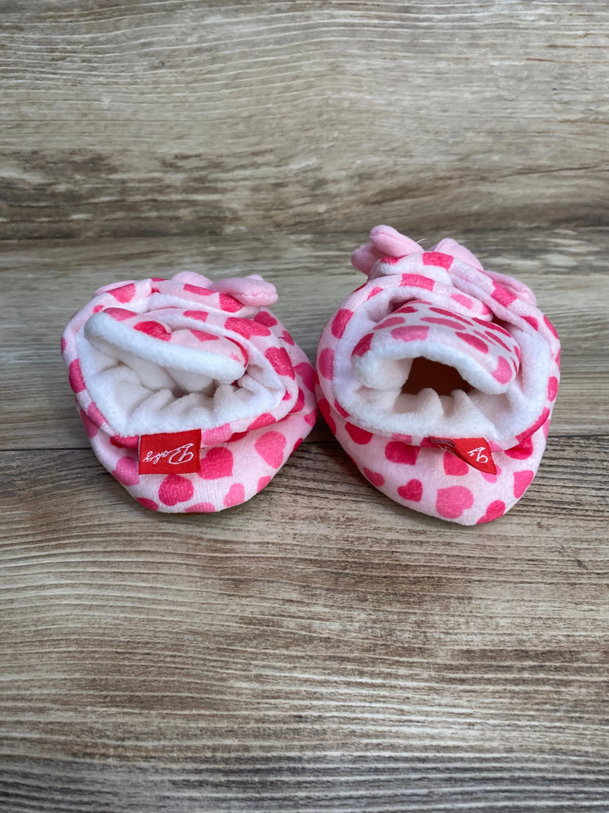 Front view of pink heart newborn cotton baby booties showing soft fleece lining and elasticized ankle cuff on wood background