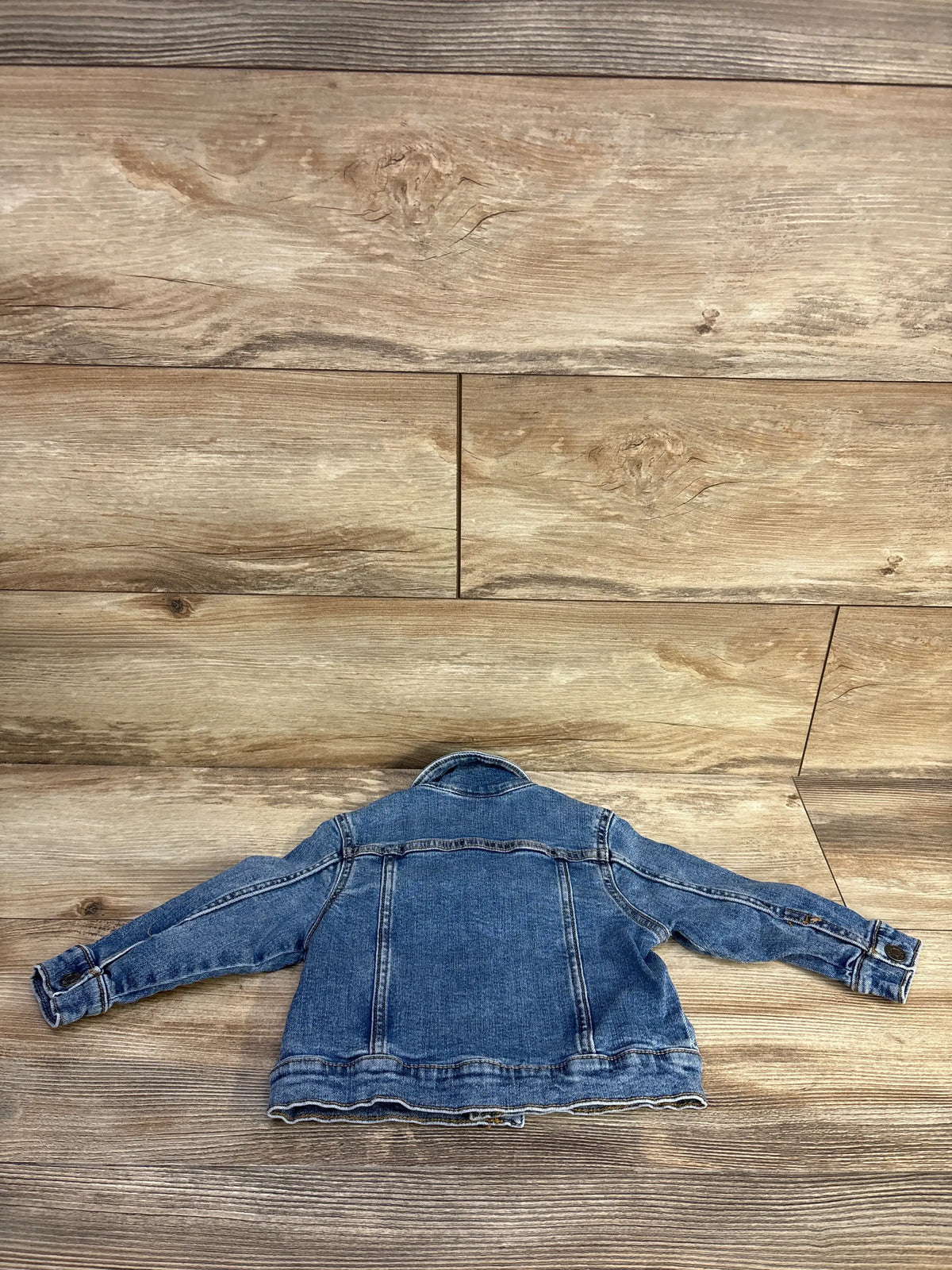 Back view of Okie Dokie blue denim jacket, size 2T, showcasing stitched panels on a wood surface