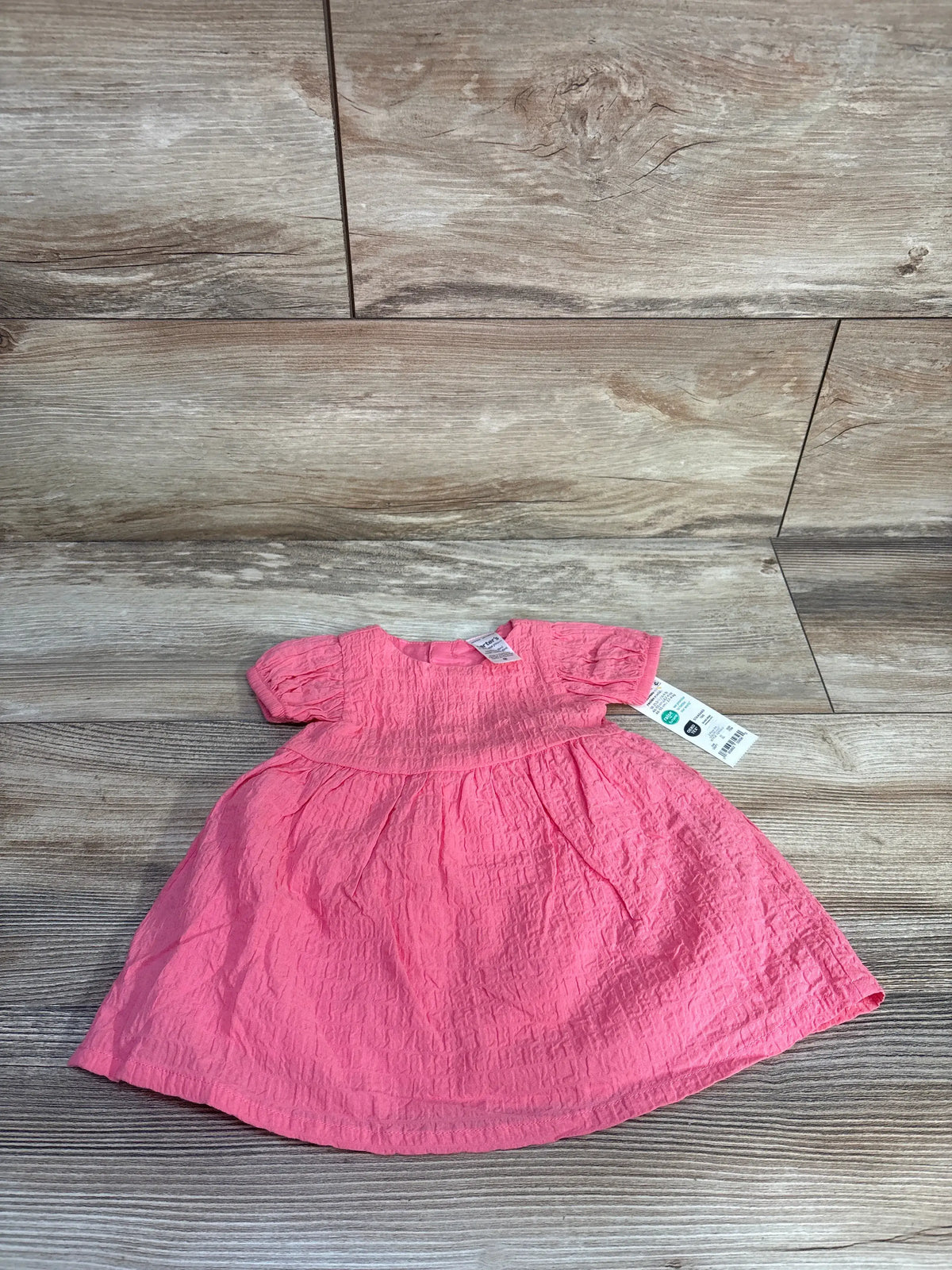 Front view of newborn pink crinkled dress with short puff sleeves and gathered skirt laid flat on wood background