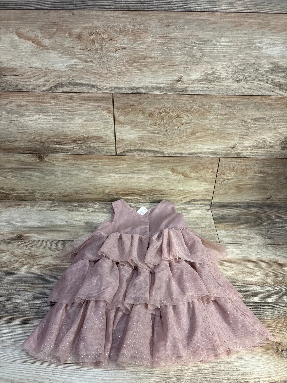 Front view of H&M sleeveless layered tulle dress in pink showcasing tiered ruffles and dotted tulle on a wood-look floor