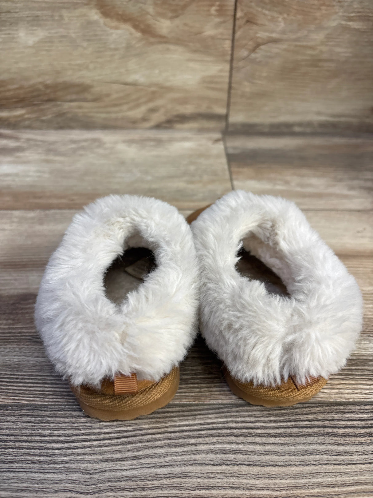 Top view of toddler slippers size 5C showing cream faux fur trim and brown sole on light wood background