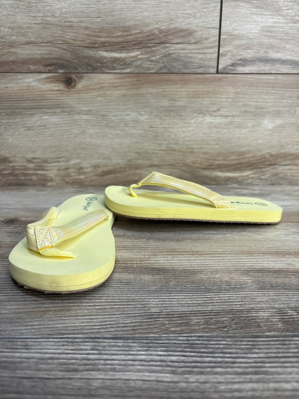 Side view of Cat & Jack Ava toddler yellow flip-flops showcasing textured iridescent straps on wood background