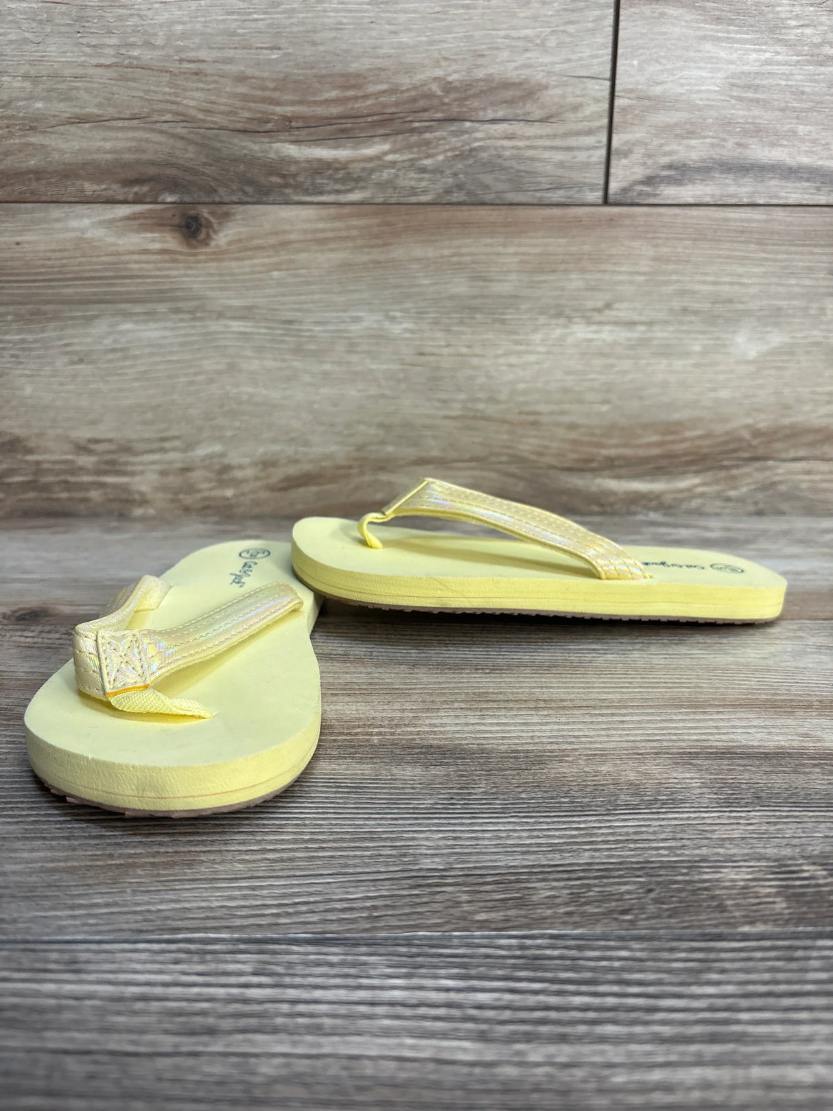 Yellow children's flip flops with textured straps on wood background