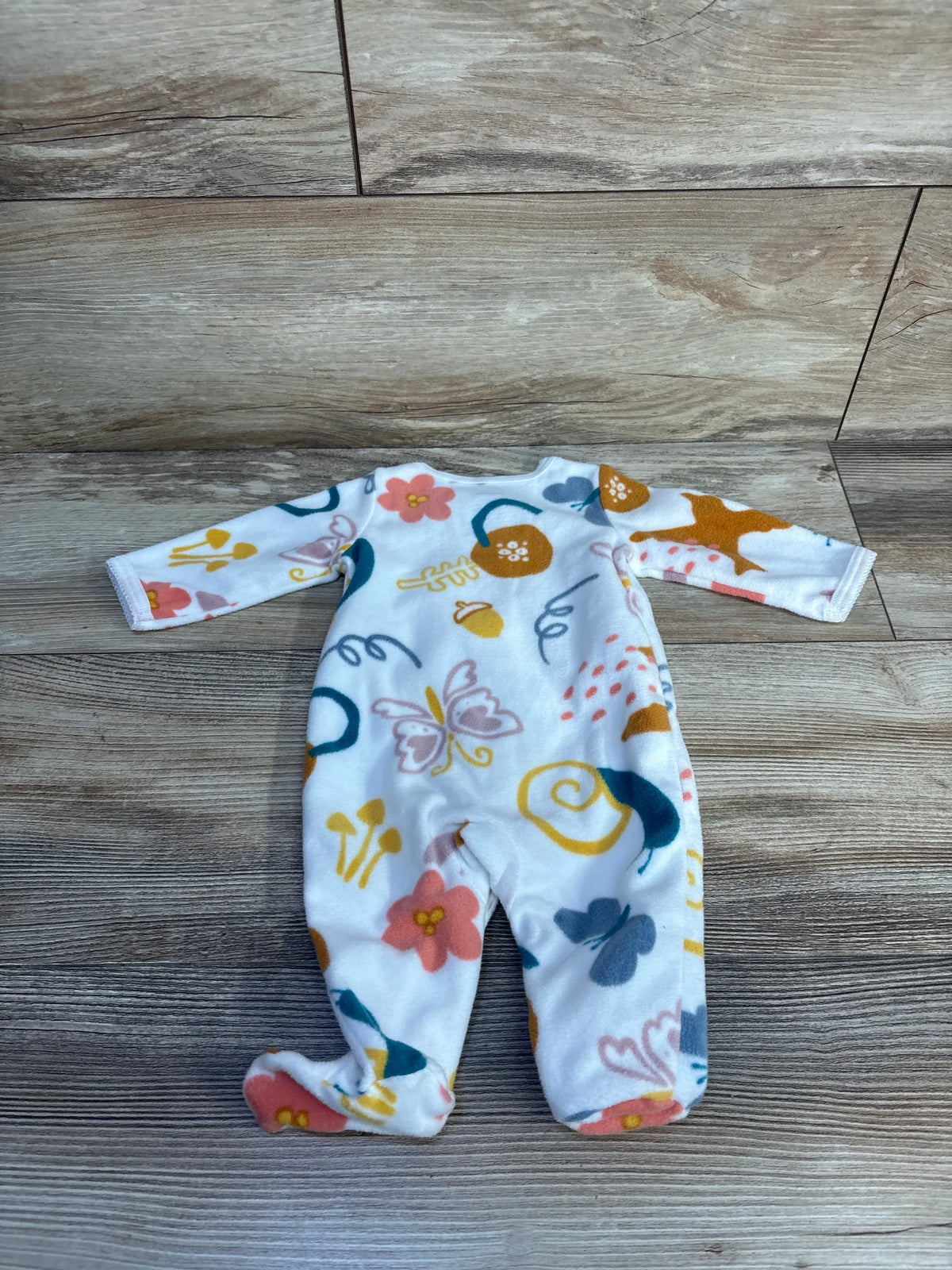 Front view of Carter’s white newborn snap blanket sleeper showcasing multicolor print and footed legs on wood-look floor