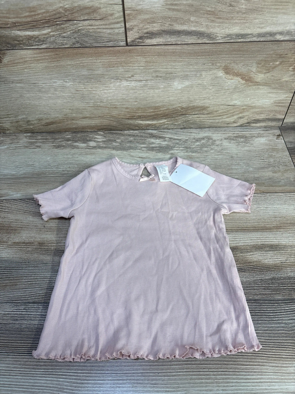 Front view of H&M pink ribbed shirt showcasing lettuce trim on the sleeves, neckline, and hem with a wood-look background
