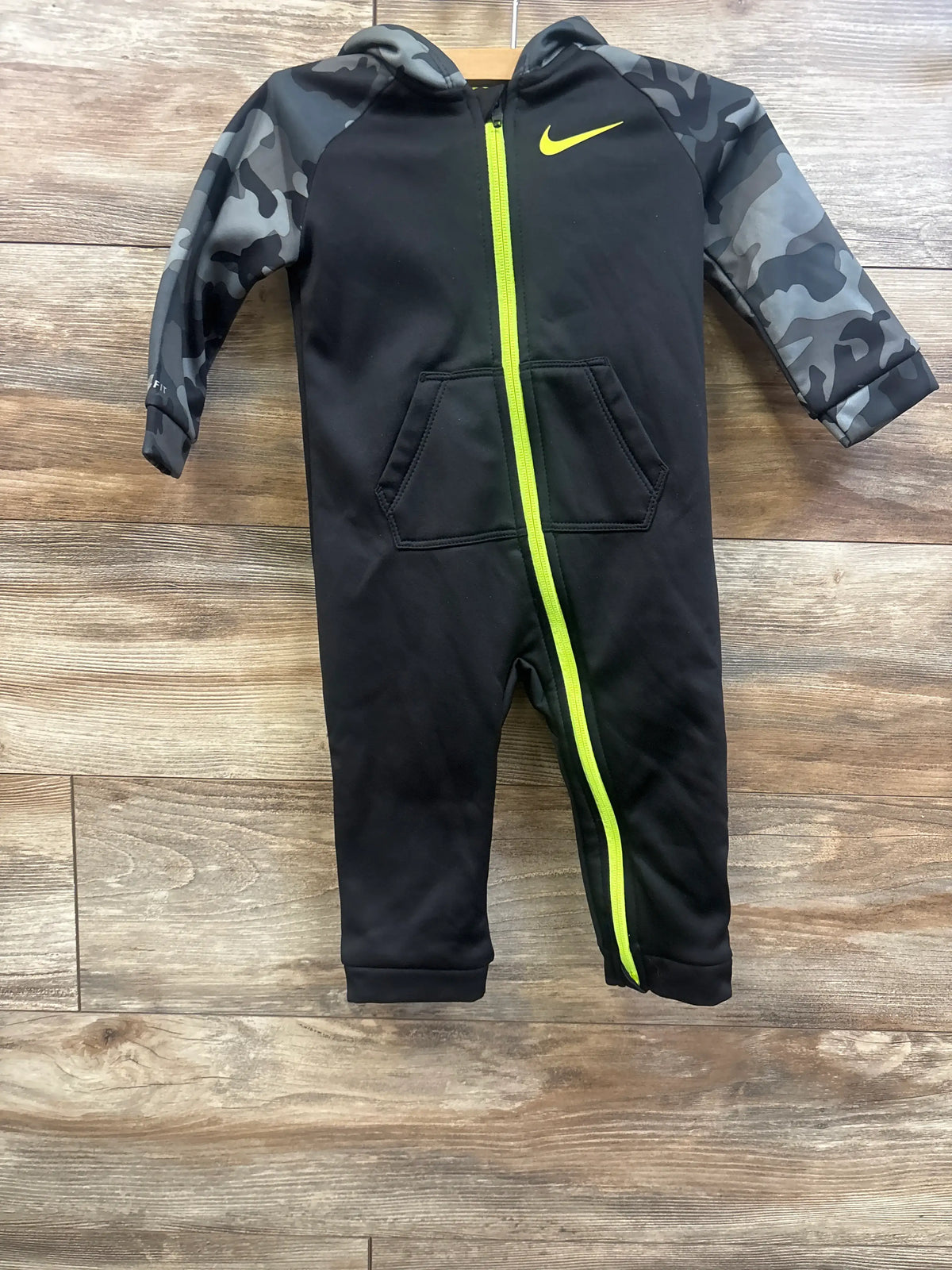 Front view of Nike Therma Fit hooded coverall, black with camo sleeves, neon zipper and pockets on wood floor, size 18 months