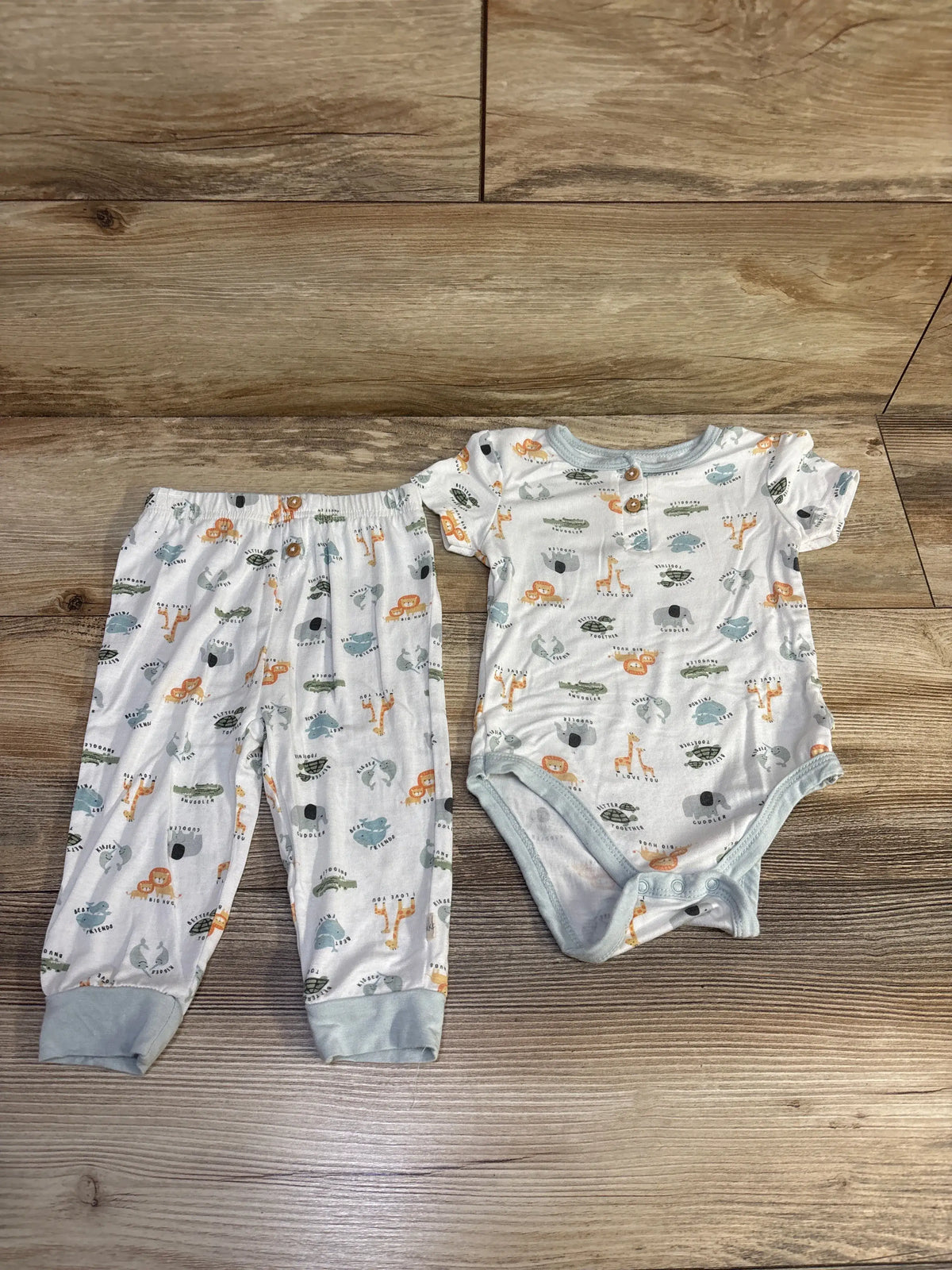 Top-down view of Milkberry 2pc bamboo animal bodysuit and pants set in white with animal print and gray trim on wood floor