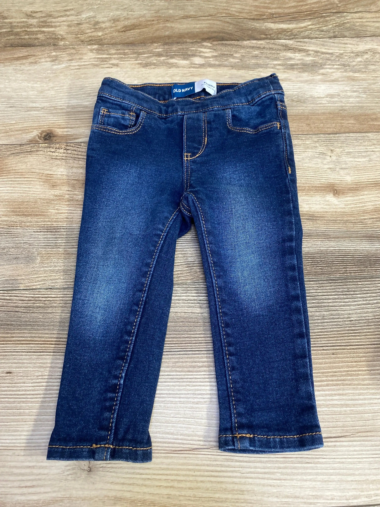 Front view of Old Navy toddler skinny jeans, dark blue, 18-24 months, elastic waist and faux pockets on wood background