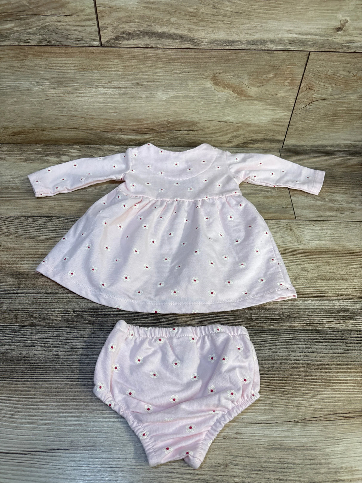 Pink baby dress and bloomers set with small white floral print on wood floor
