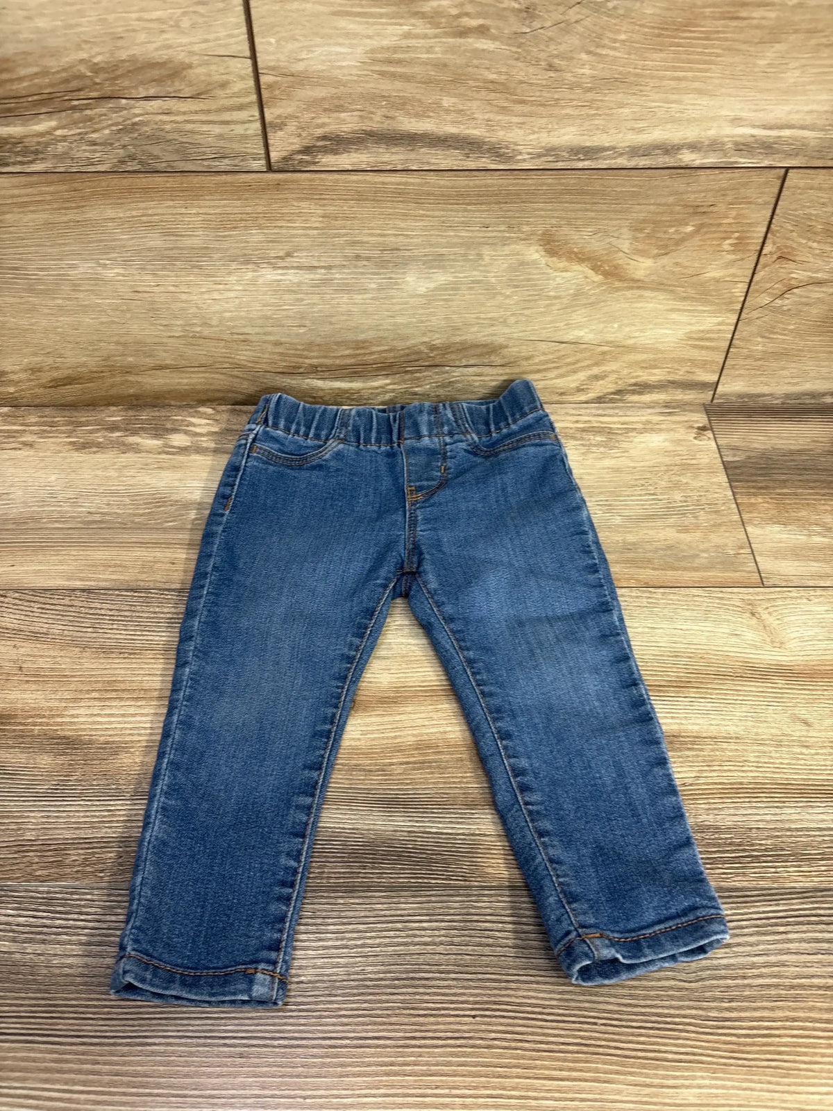 Front view of OshKosh blue toddler jeggings size 18 months showing elastic waistband and slim legs on a wood floor background