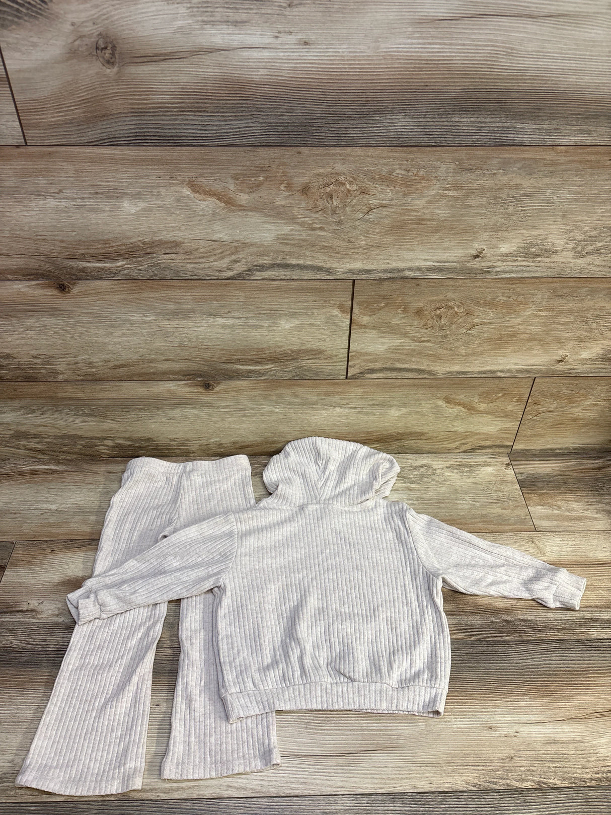 Top-down view of light gray ribbed baby hoodie and matching pants set showcasing ribbed texture and hood on wood background