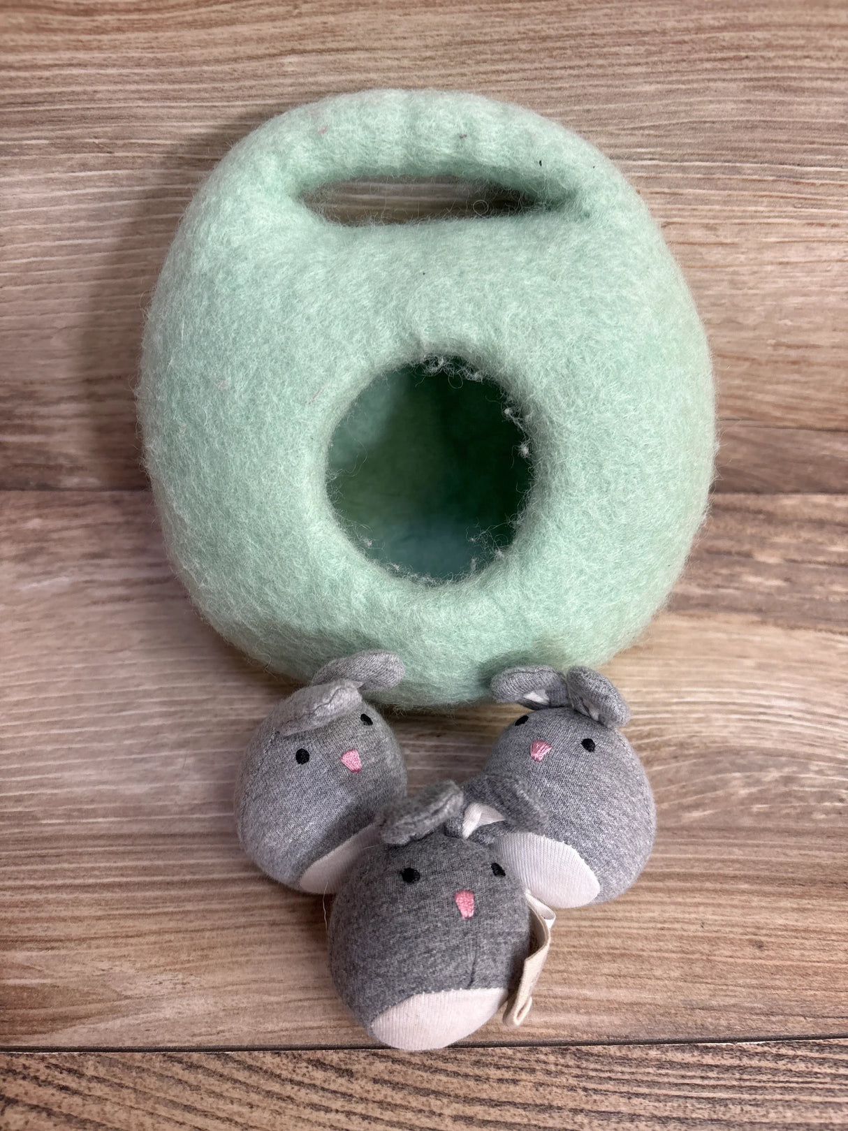 Soft mint green felted toy basket with three gray plush bunny toys on wood background