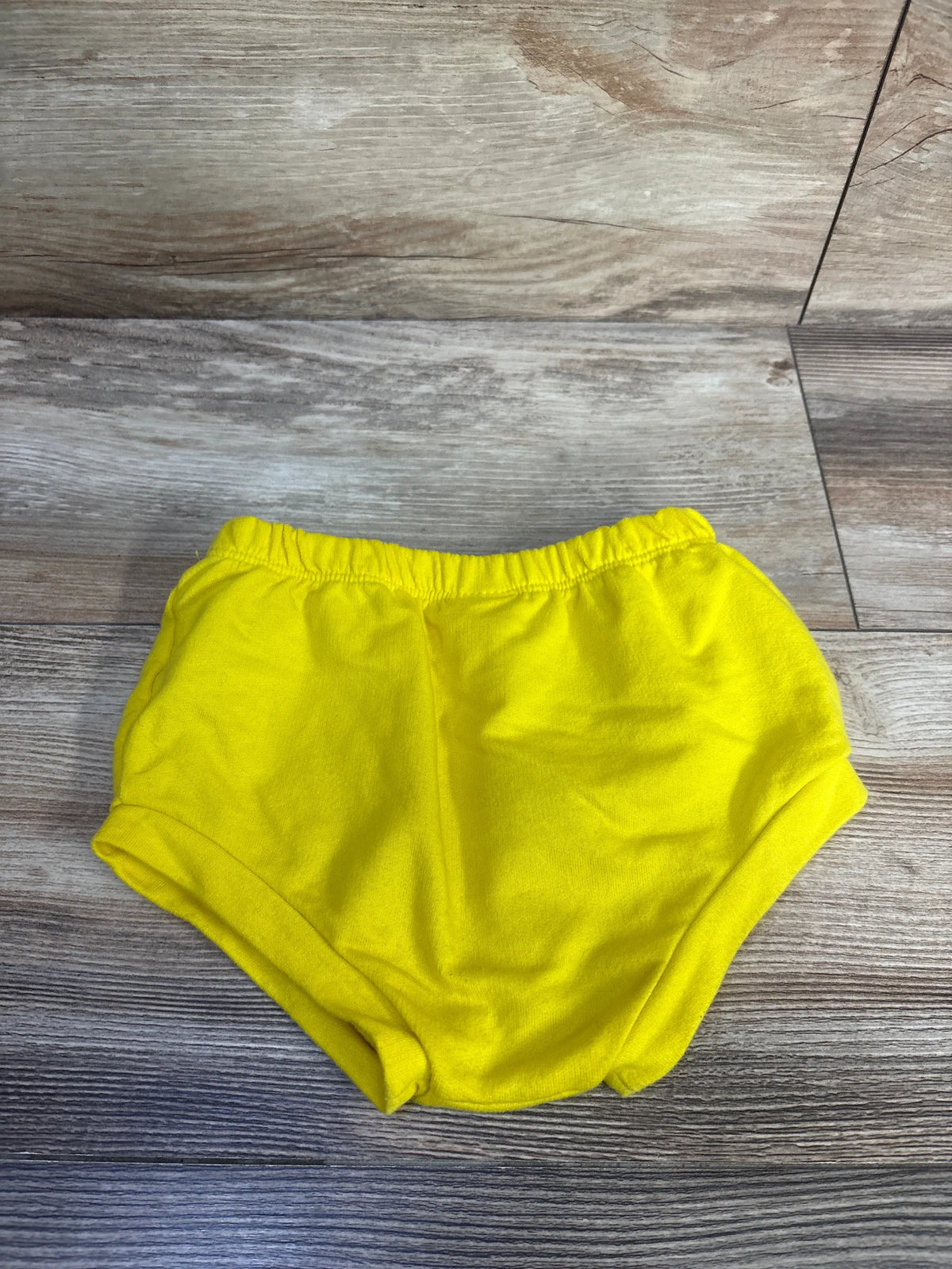 Front view of Cat and Jack yellow bloomers showcasing elastic waistband and leg openings on a wood grain floor