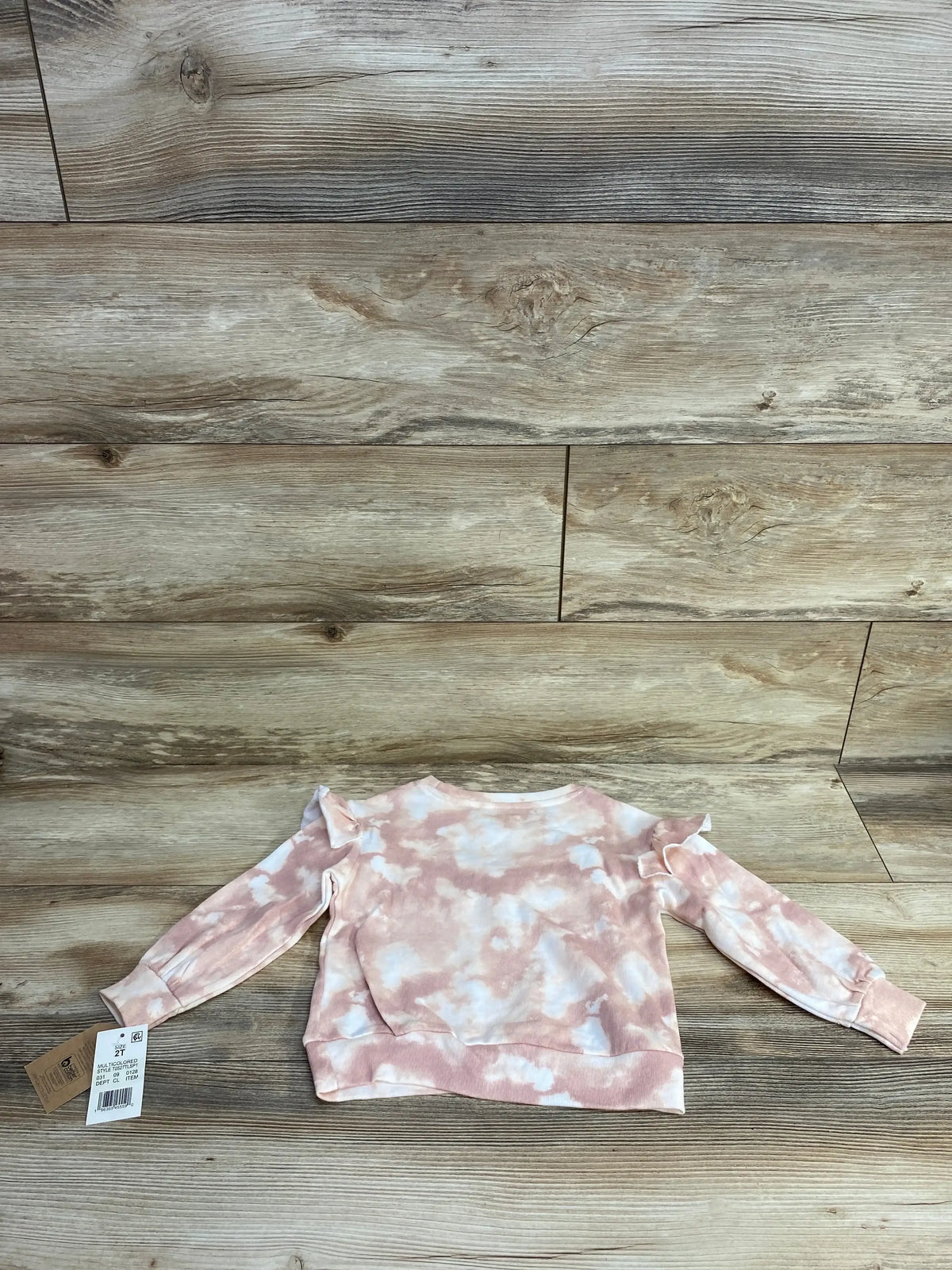 Toddler pink and white tie-dye long sleeve sweatshirt with ruffle shoulder detail on wood background