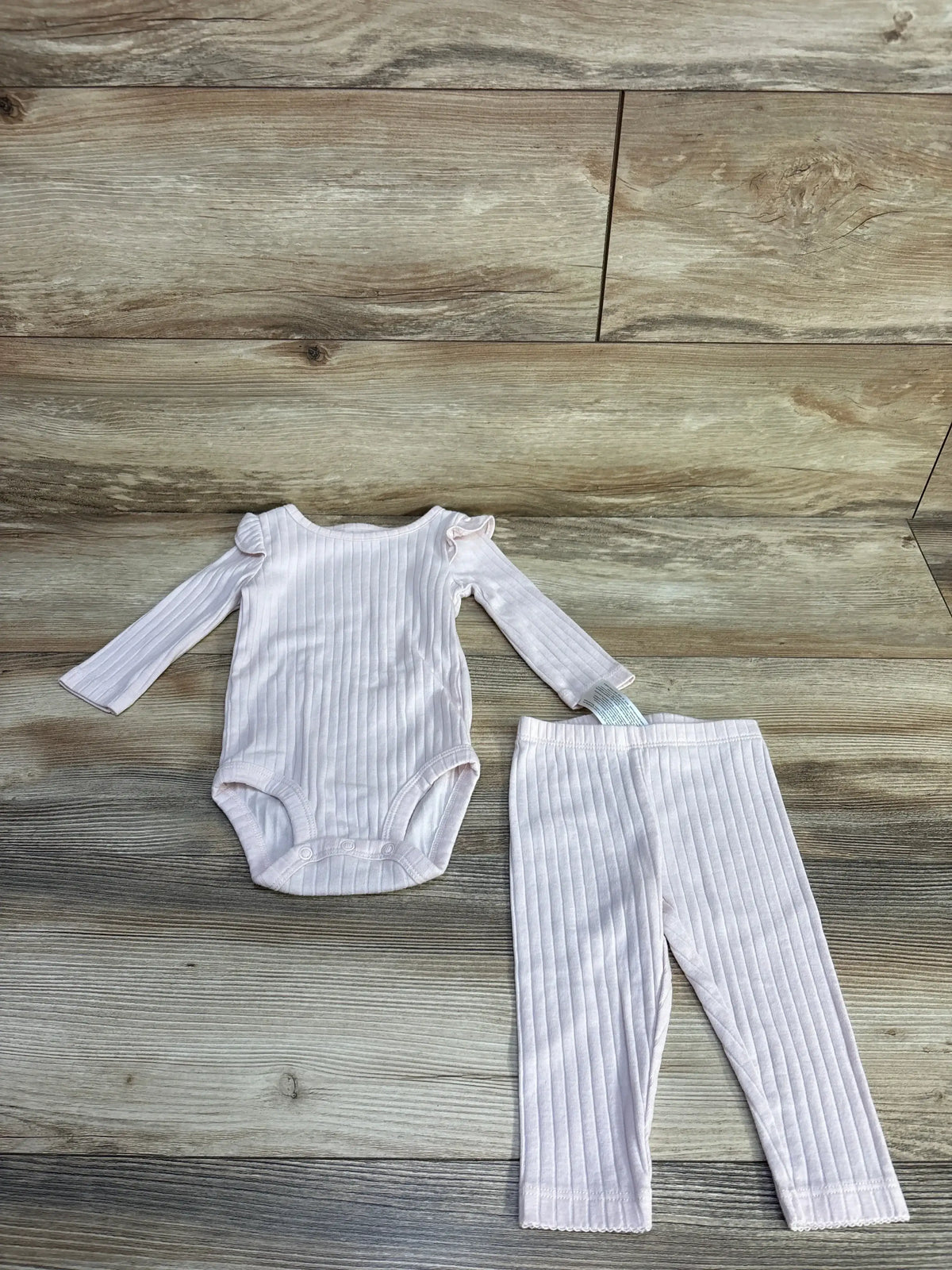 Flat lay of Carter’s pink ribbed 2-piece baby set: long-sleeve ruffle-shoulder bodysuit and matching leggings on wood background