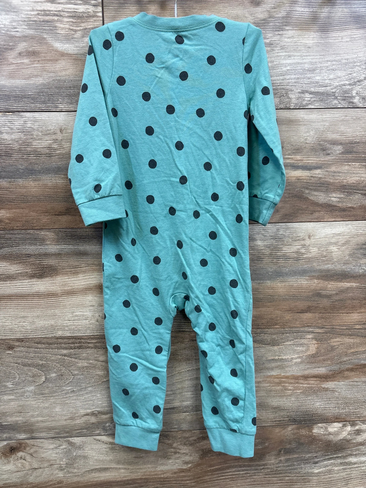 Teal long sleeve baby romper with black polka dots on rustic wood background
