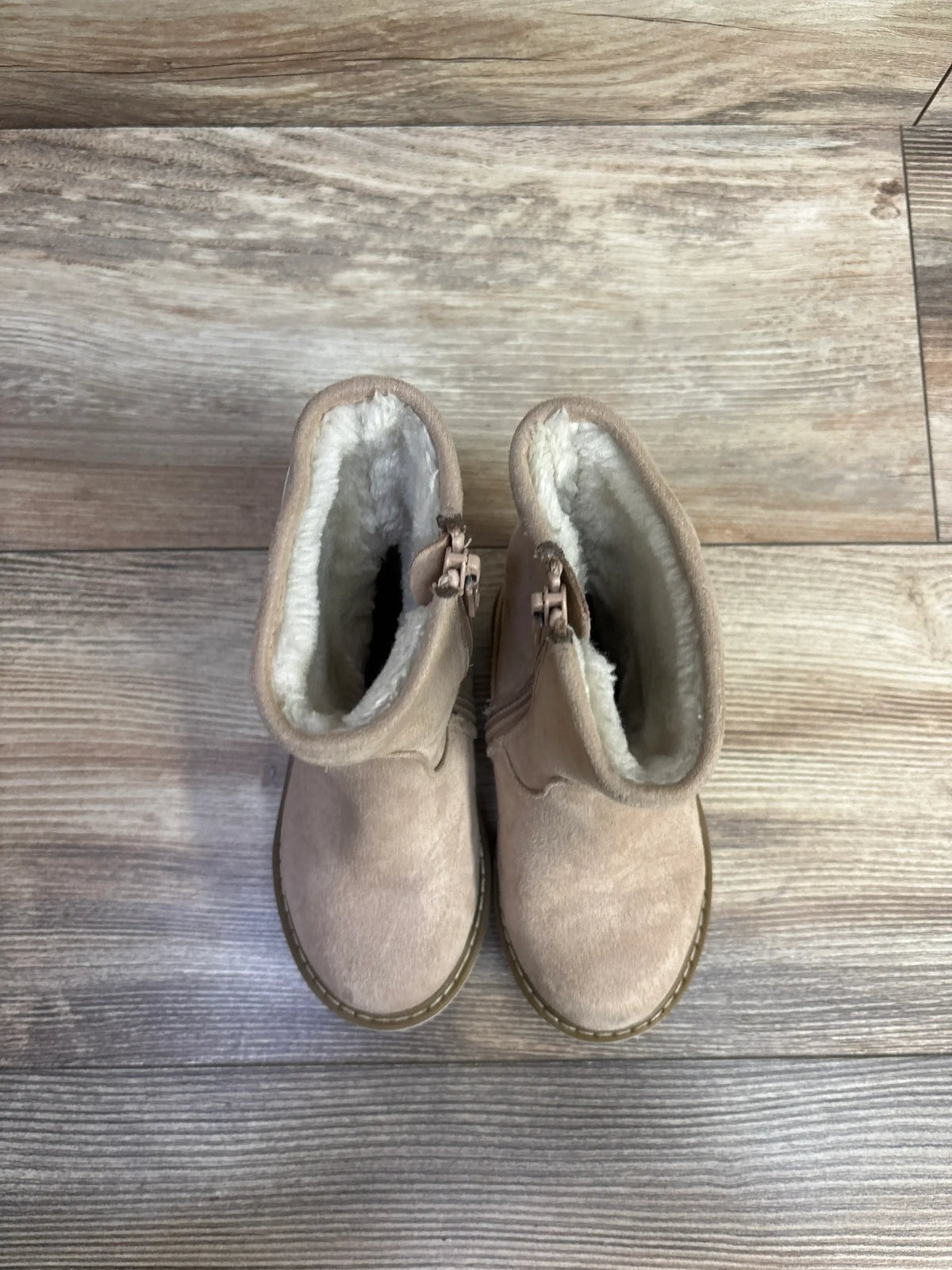 Top-down view of tan suede toddler winter boots with cream faux fur lining and side zippers on wood plank floor