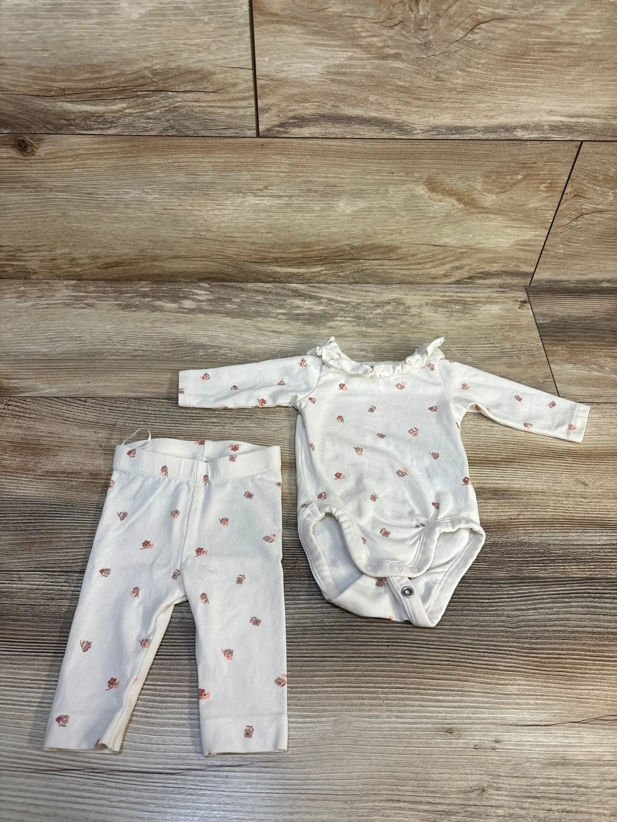 White baby onesie and pants set with small pink floral print on wood background