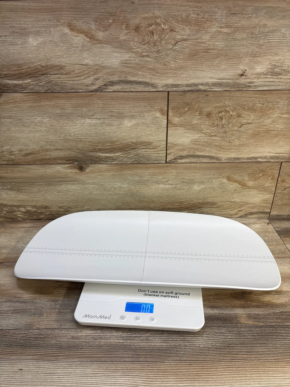 Front view of MomMed Baby Scale showcasing height markings and digital display with a wood-look floor background