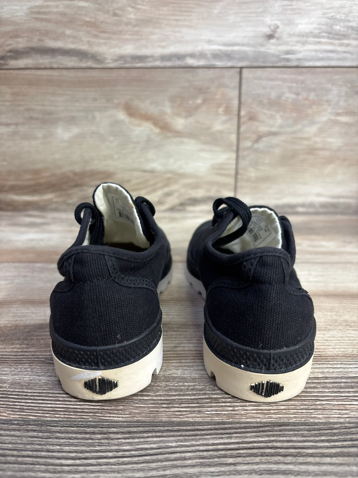 Pair of black toddler sneakers with white soles on wooden floor background