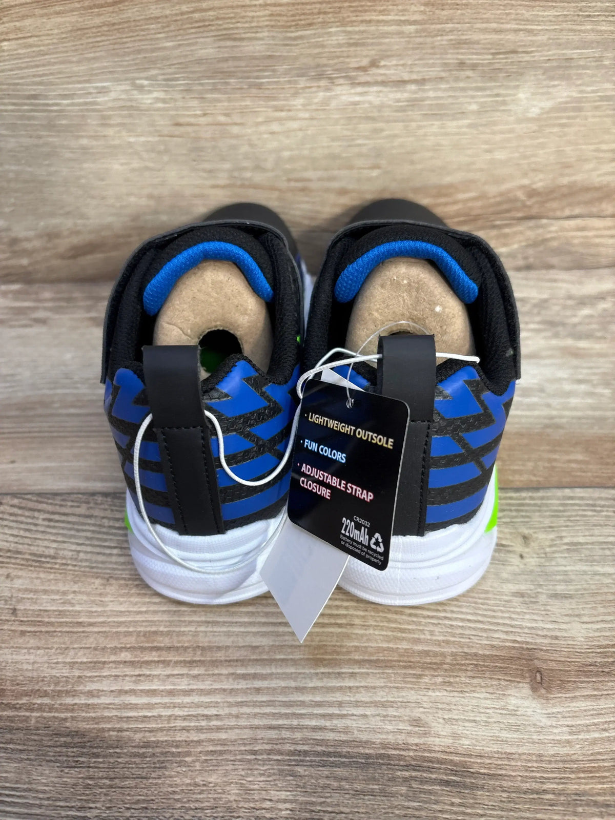 Back view of S Sport Skechers Lights Ottis toddler sneakers with black upper, blue heel accents, pull tab and hangtag on wood floor