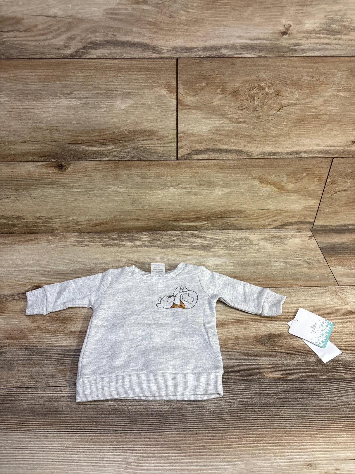 Front view of newborn grey Winnie the Pooh sweatshirt with chest embroidery and long sleeves on wood background