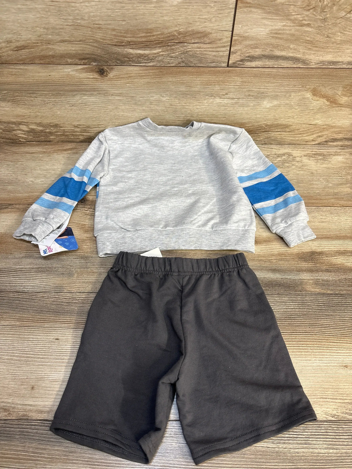 Kids’ outfit with gray long sleeve shirt blue striped sleeves and black shorts on wood floor