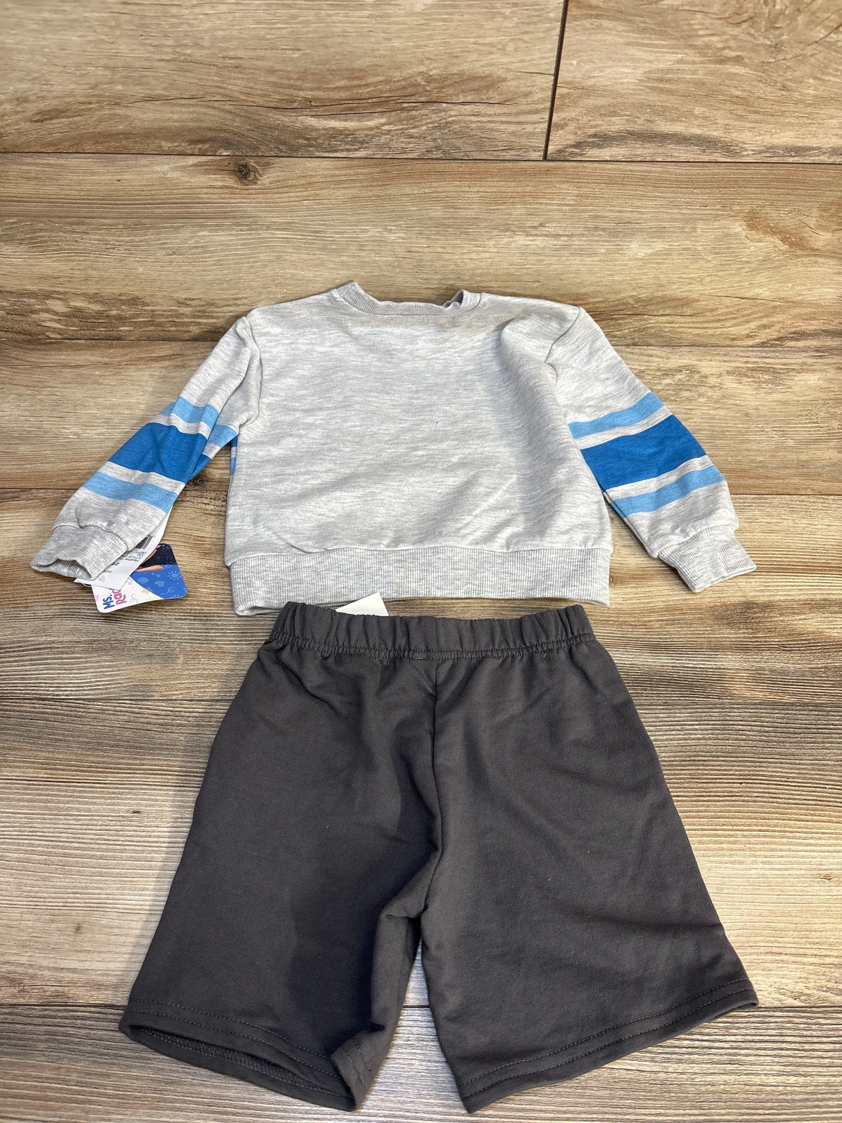 Kids’ outfit with gray long sleeve shirt blue striped sleeves and black shorts on wood floor