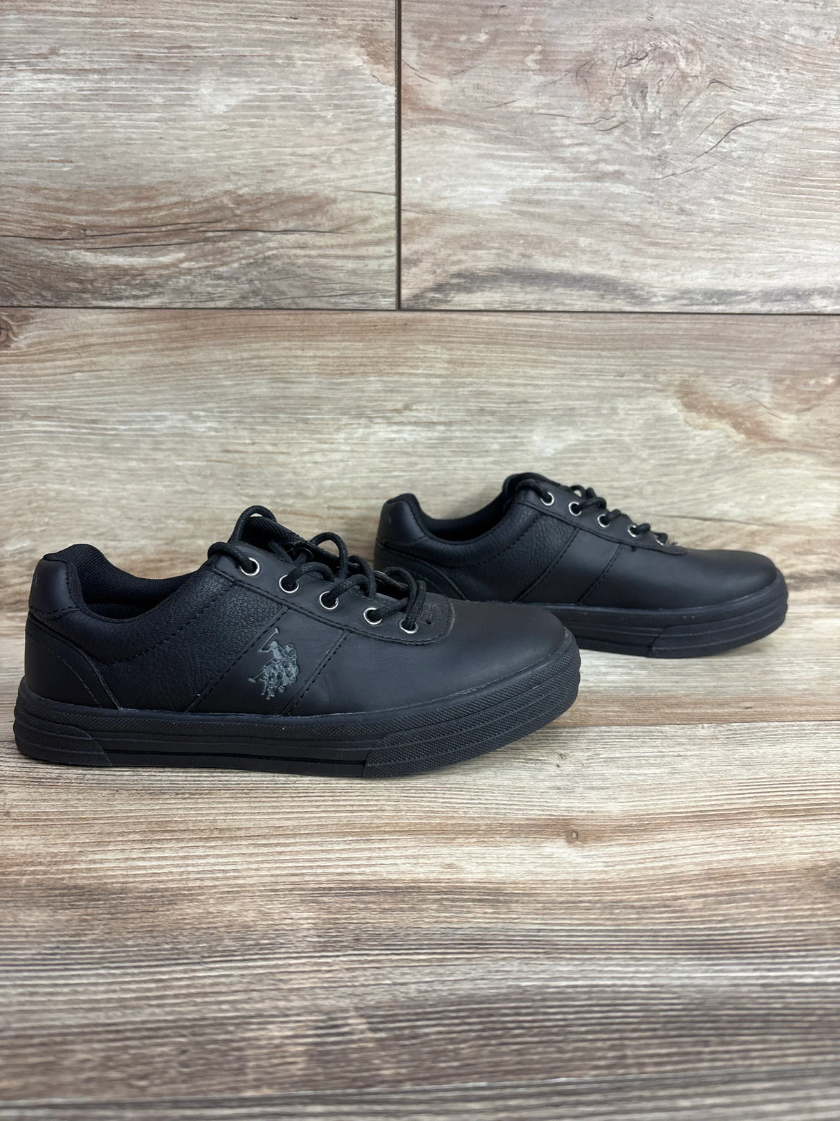 Black kids low top sneakers with lace-up closure and side logo on wood background