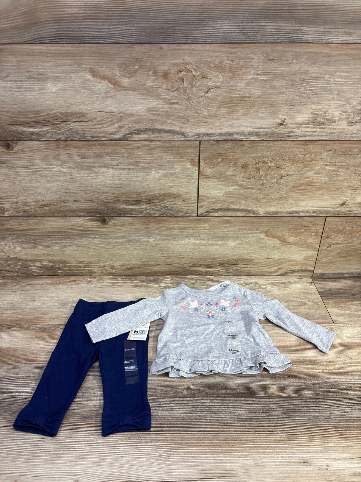 Flat lay of gray peplum long sleeve baby top with floral embroidery and navy pants with bow cuffs on wood background