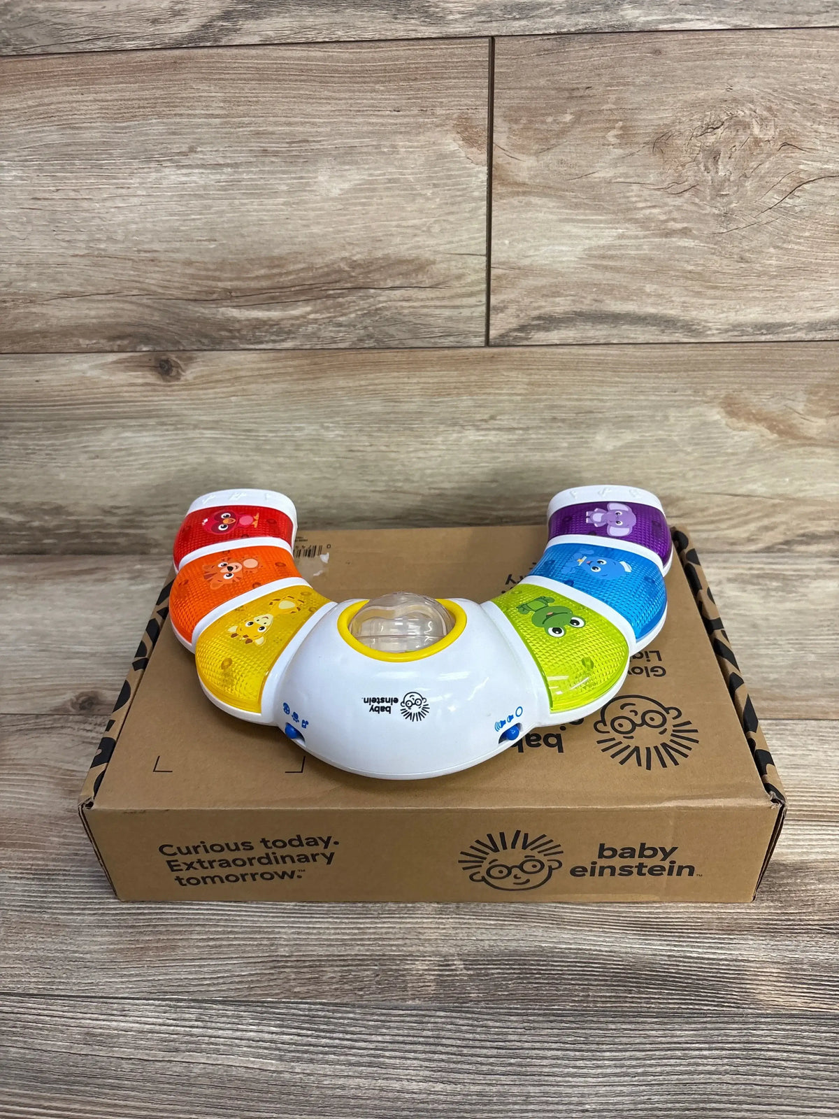 Front view of Baby Einstein Glow & Discover Light Bar showing rainbow animal light-up buttons on box on wood surface