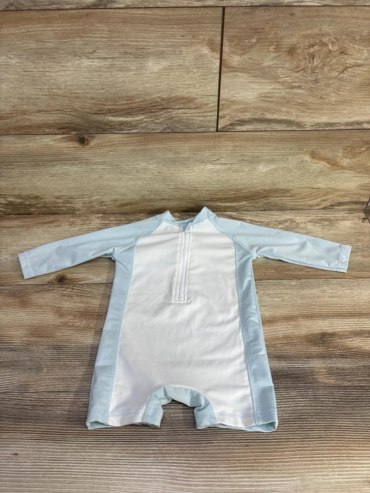 Front view of Cuddle Cubs one-piece rash guard in light blue for 12 to 18 months, with long sleeves and half zipper on wood